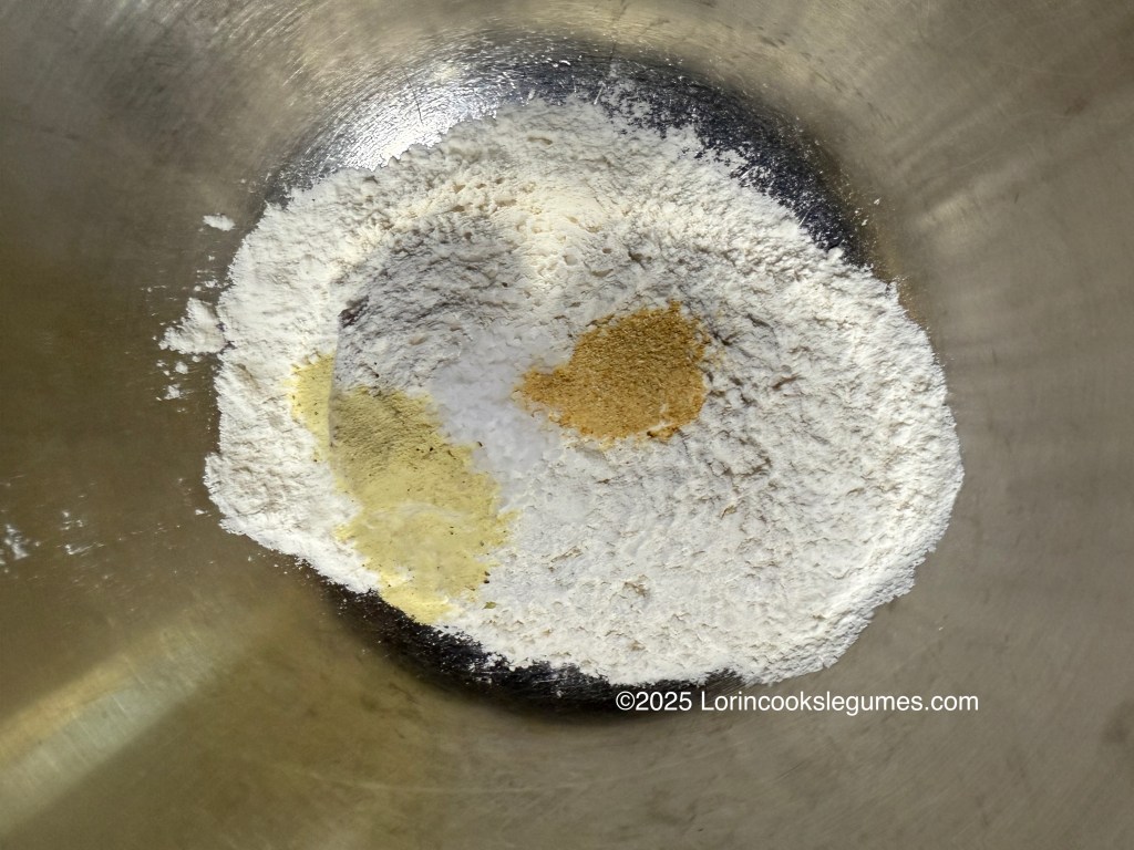 A close-up view of a mixing bowl containing flour and various spices, including garlic powder and adobo seasoning, ready for preparing dumplings.