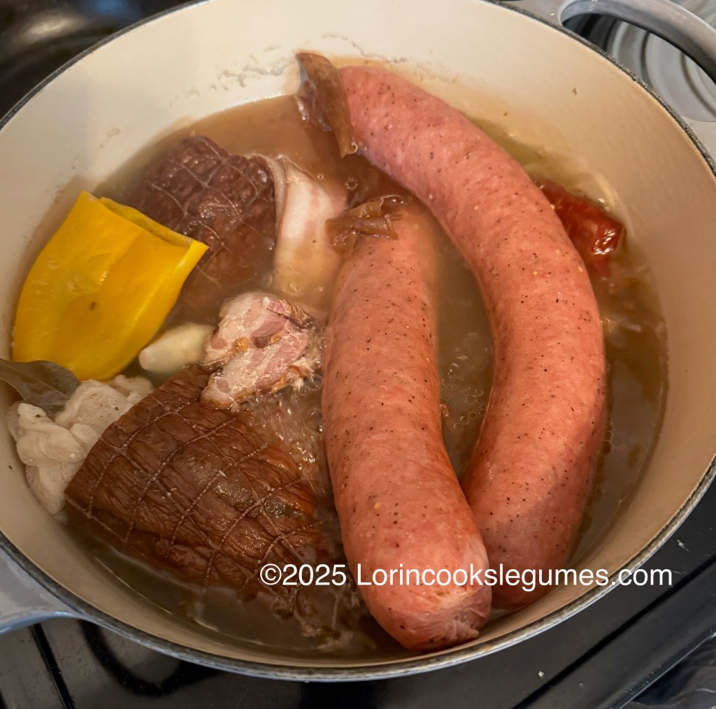 A pot filled with various smoked meats, sausage, and a yellow pepper simmering in broth, typical of the Slovak bean soup Fazulovica.