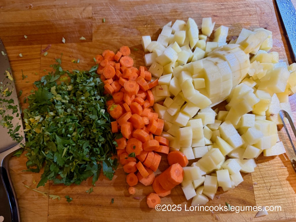Chopped vegetables including carrots and potatoes, along with finely chopped parsley, arranged on a wooden cutting board next to a knife.