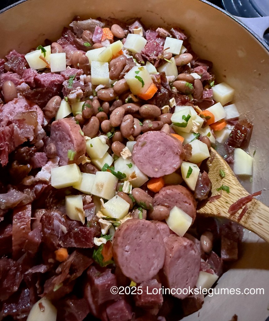 A pot filled with ingredients for Fazulnica, featuring various smoked meats, pinto beans, diced potatoes, carrots, and chopped herbs, stirred with a wooden spoon.