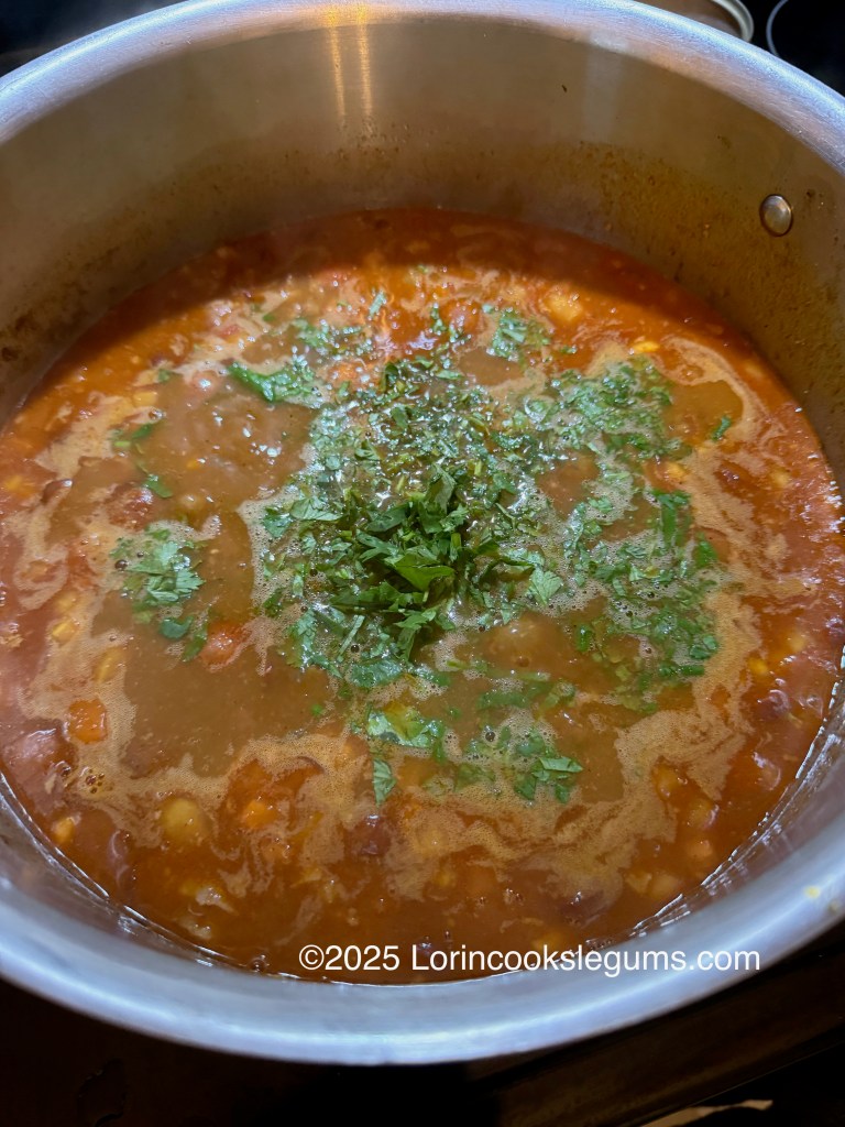A pot of frijoles charros (cowboy beans) simmering, with a broth with a rich reddishcolor and topped with freshly chopped cilantro.