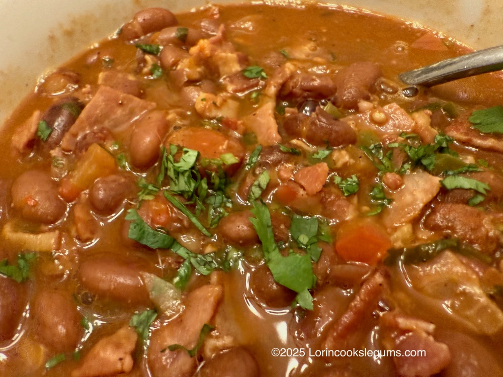 Close-up of a bowl of frijoles charros, a traditional Mexican dish, featuring pinto beans, bacon, diced tomatoes, and fresh cilantro, all in a savory broth.