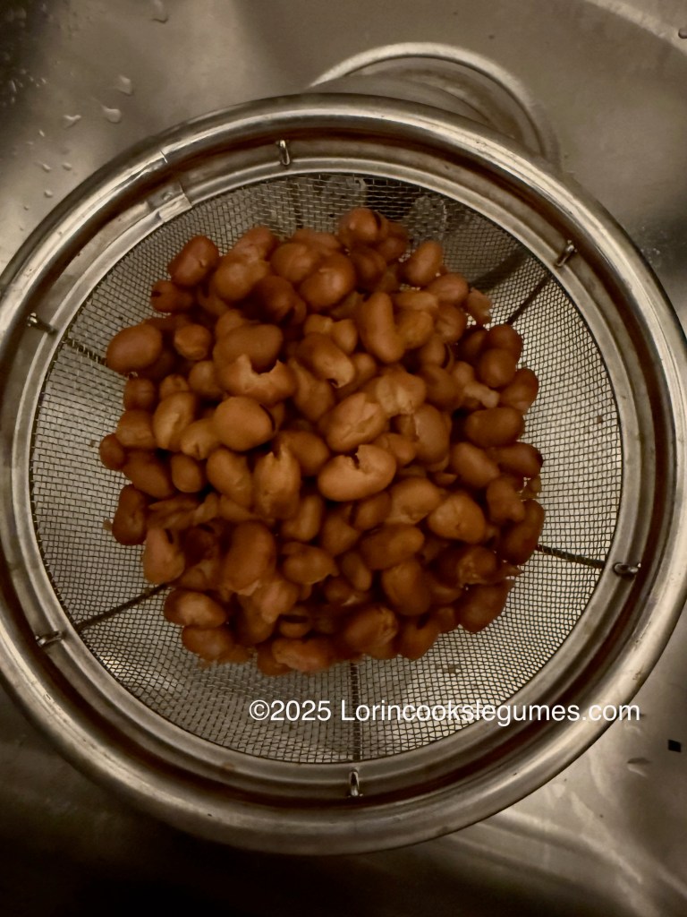 A colander filled with cooked fava beans, sitting in a sink.