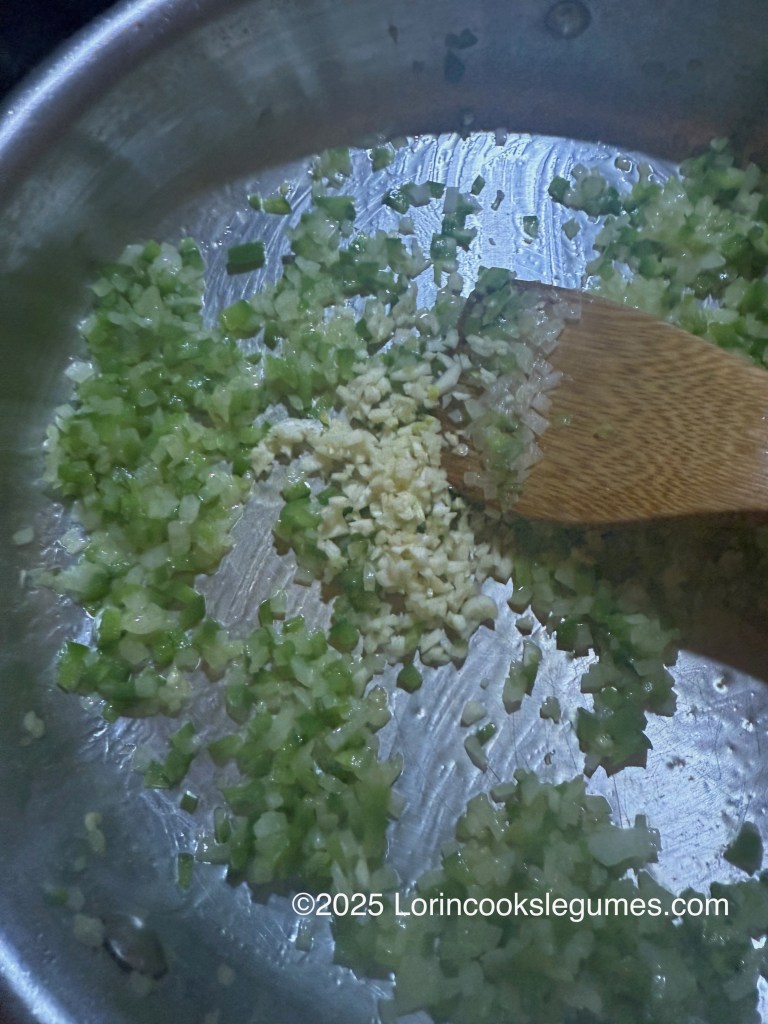 Chopped onions, peppers, and minced garlic sautéing in a silver pan.