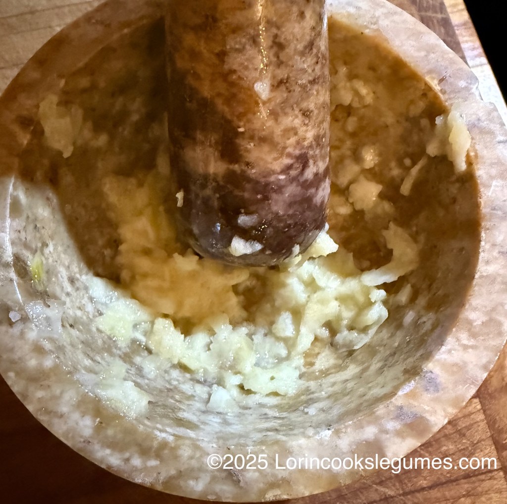 Close-up view of a mortar and pestle with garlic being mashed into a paste.