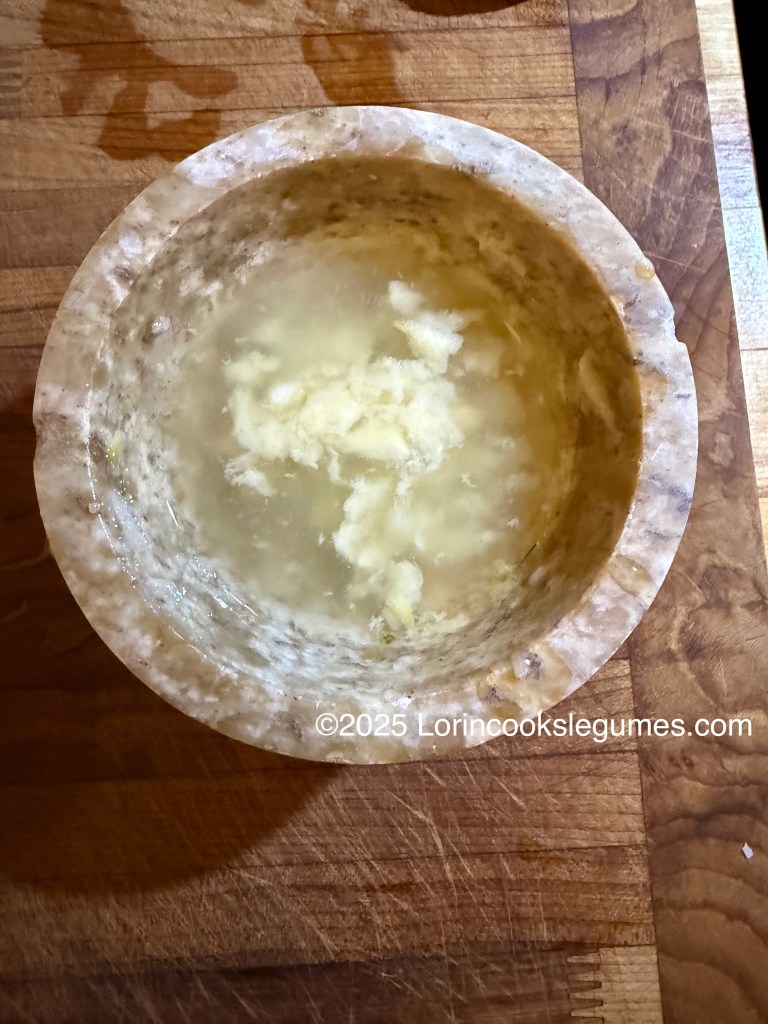 A mortar containing garlic paste and lemon juice, set on a wooden countertop.