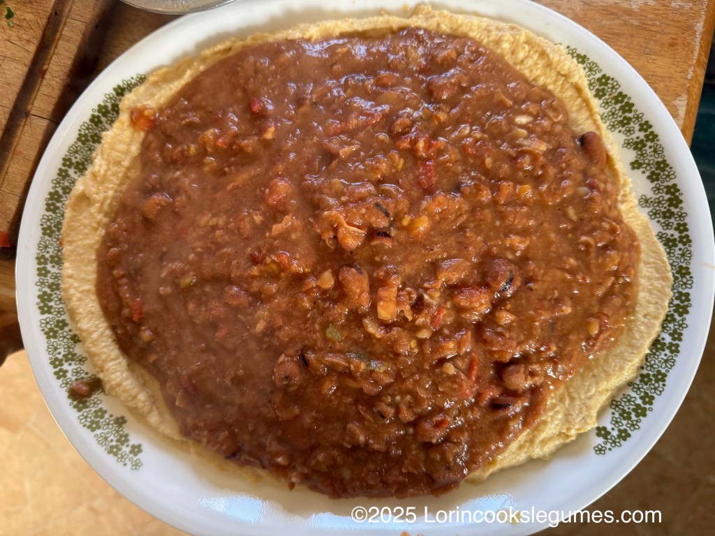 A plate featuring a layer of hummus topped with a layer of ful medames.