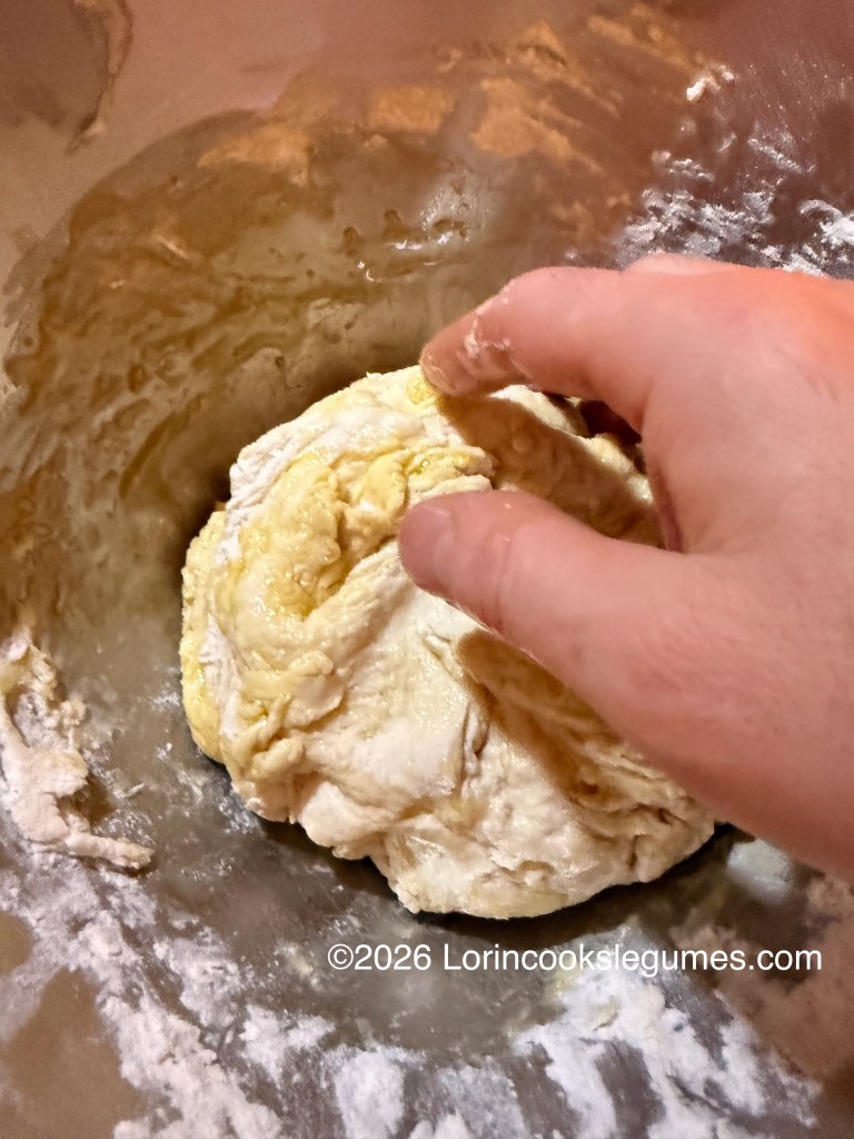 A hand kneading dough in a metal bowl coated with flour and oil.