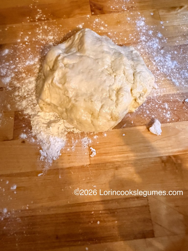 A ball of dough resting on a wooden surface, surrounded by scattered flour.