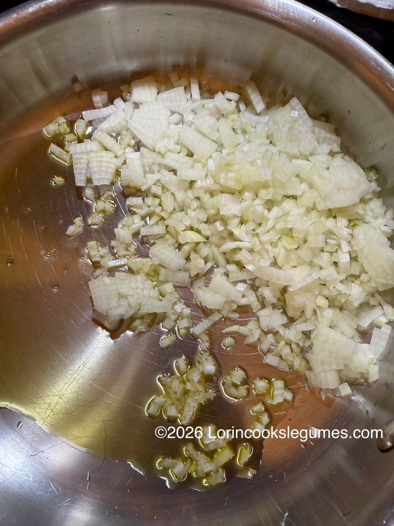 Chopped onions cooking in a stainless steel pan with olive oil.