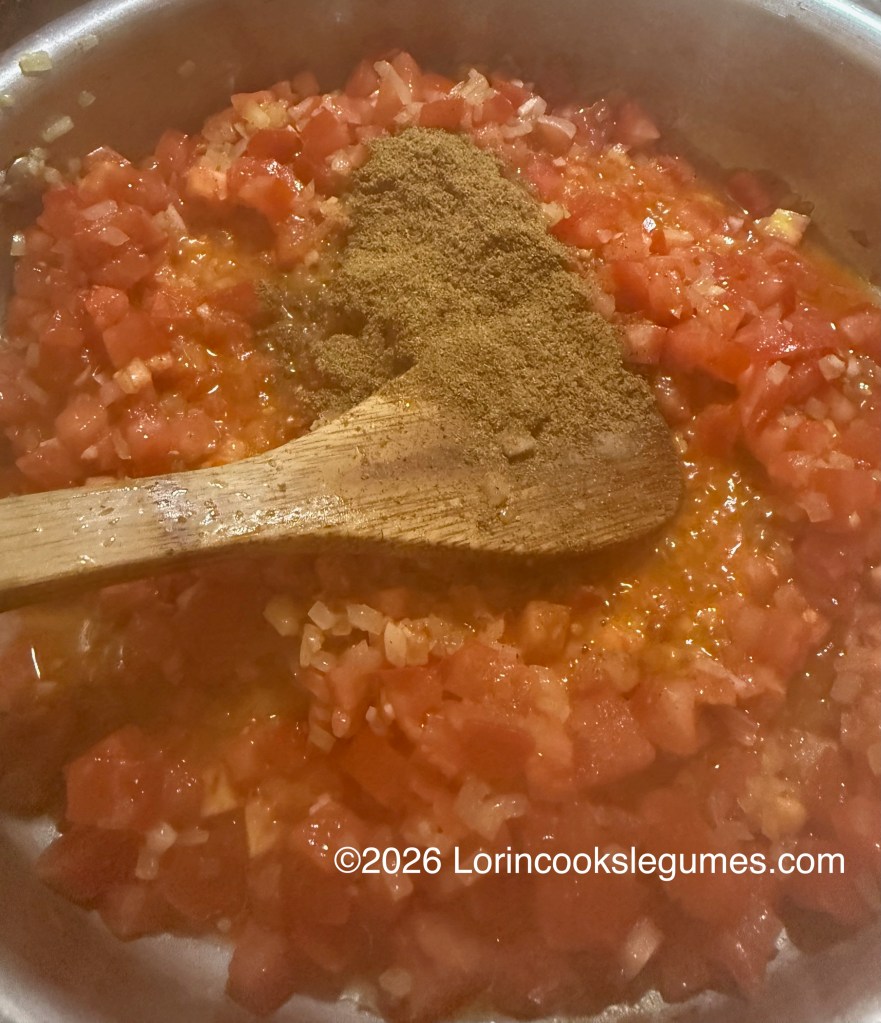 Simmering chopped tomatoes and onions with spices in a saucepan, stirred with a wooden spoon.