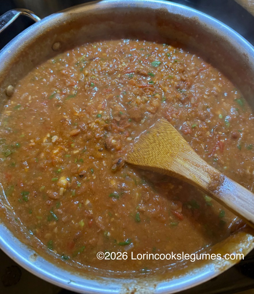 A close-up view of a pot filled with a thick, hearty bean stew, featuring a wooden spoon stirring the mixture.