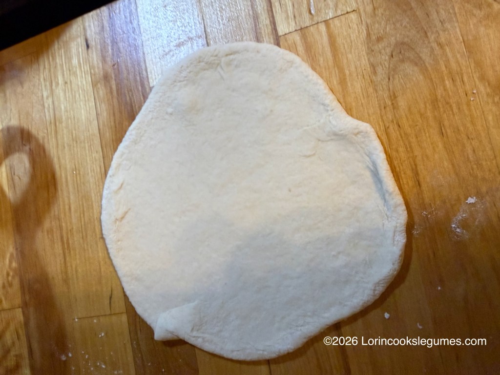 A round, flattened piece of dough resting on a wooden surface.