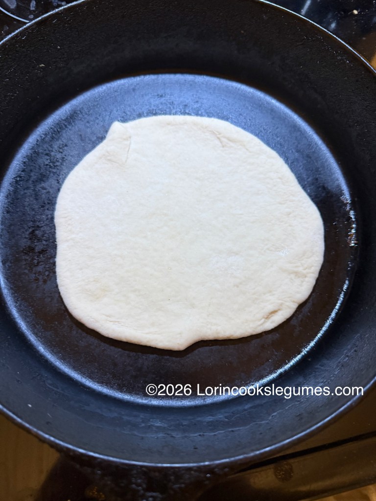 A round of raw dough placed in a cast iron skillet, ready for cooking.