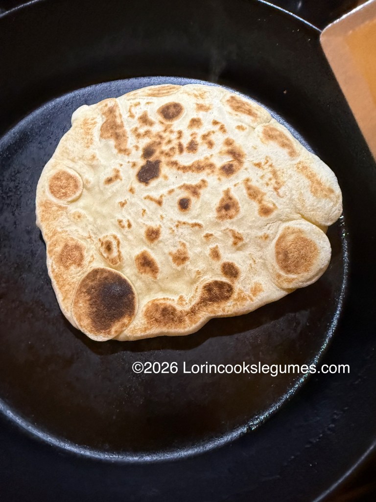 A golden-brown flatbread being cooked on a cast iron skillet.