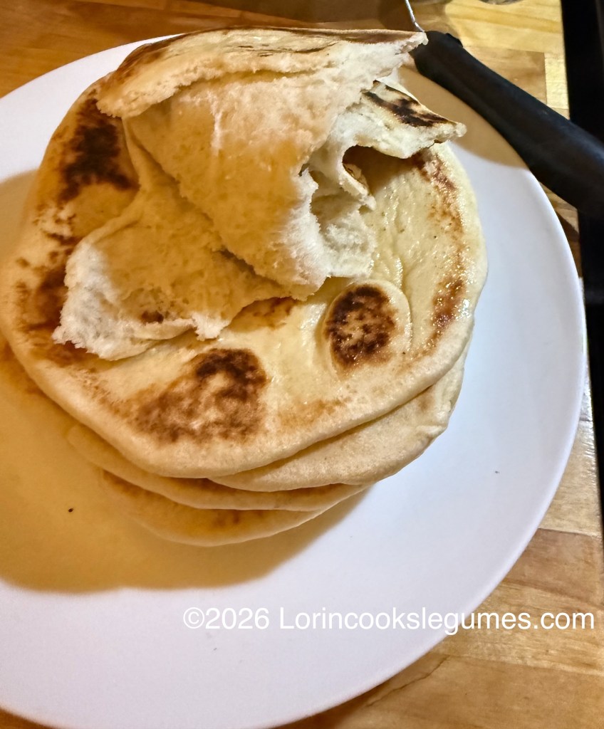 A stack of freshly made flatbreads on a white plate, with one flatbread partially folded and torn open on the top.