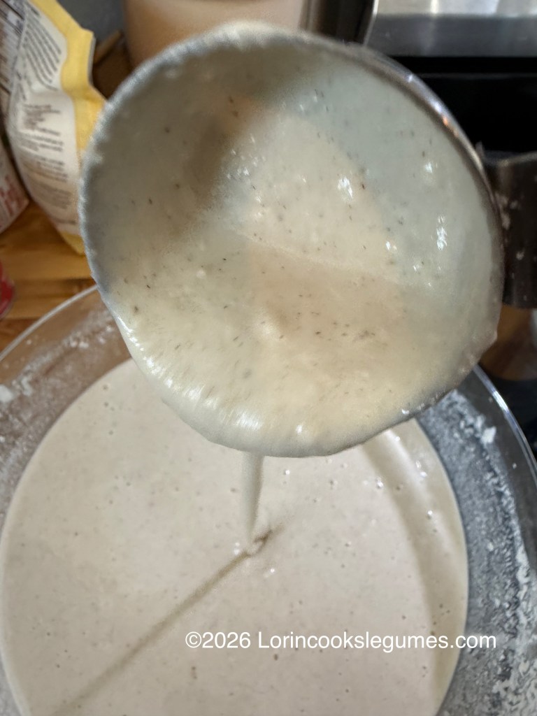 A close-up of a ladle pouring a thick batter back into a bowl of similar batter.