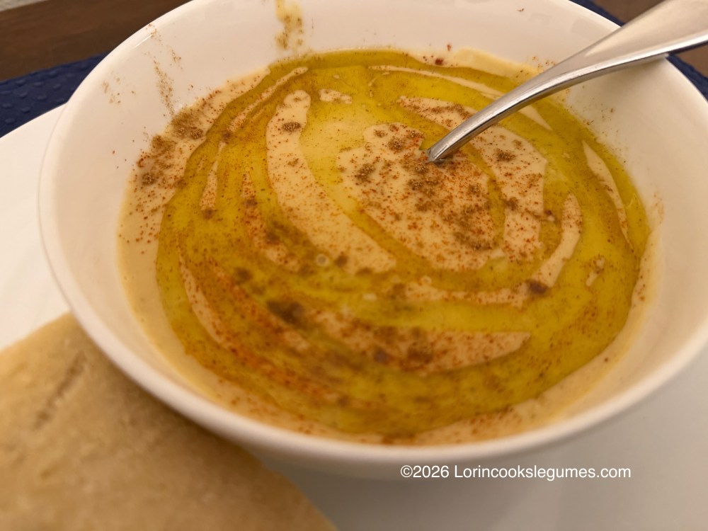 A bowl of creamy bean soup drizzled with olive oil and sprinkled with paprika, accompanied by a piece of bread.