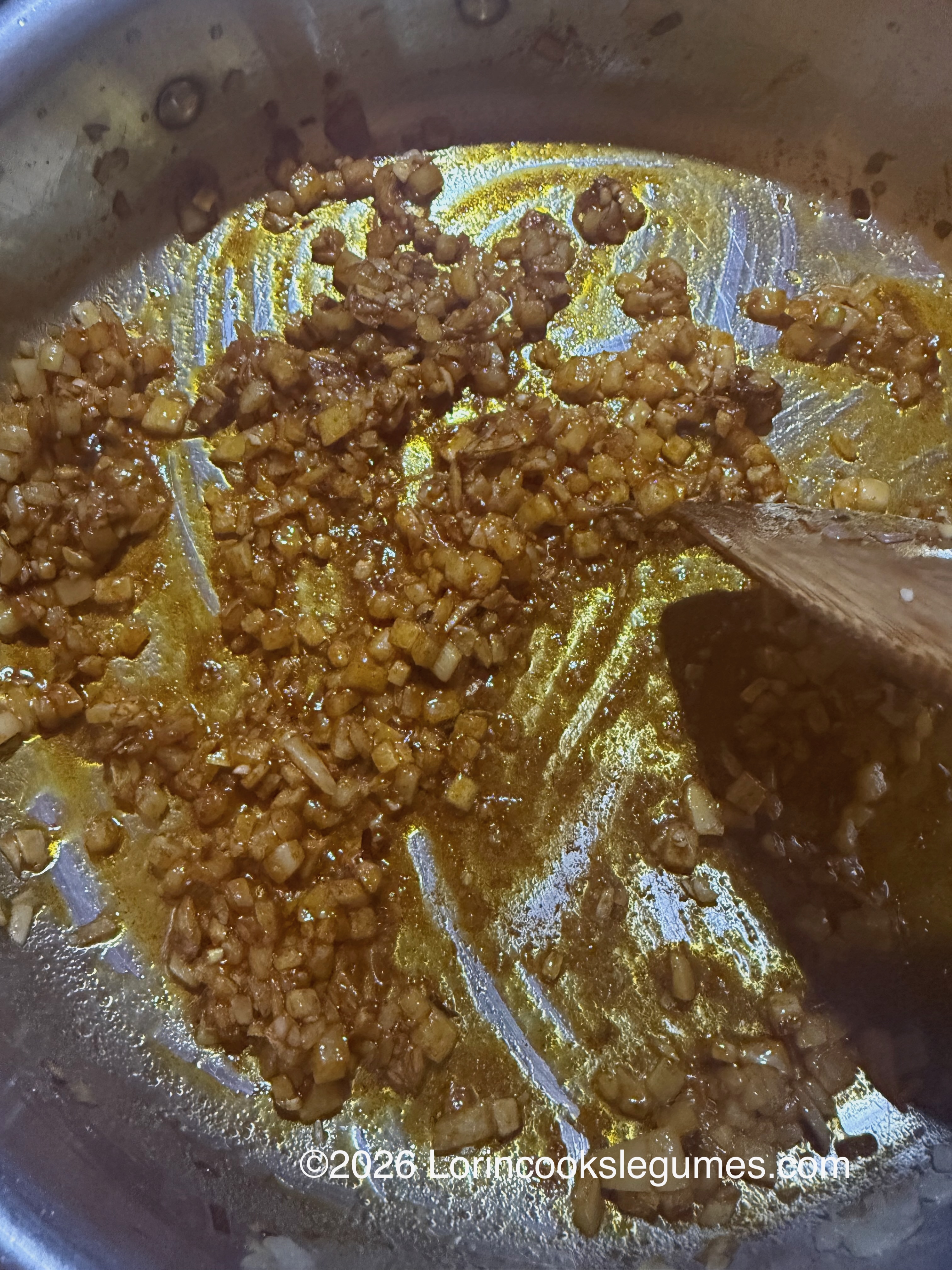 Minced onions and spices sautéing in a pan with a wooden spatula. ©2026 Lorincookslegumes.com.