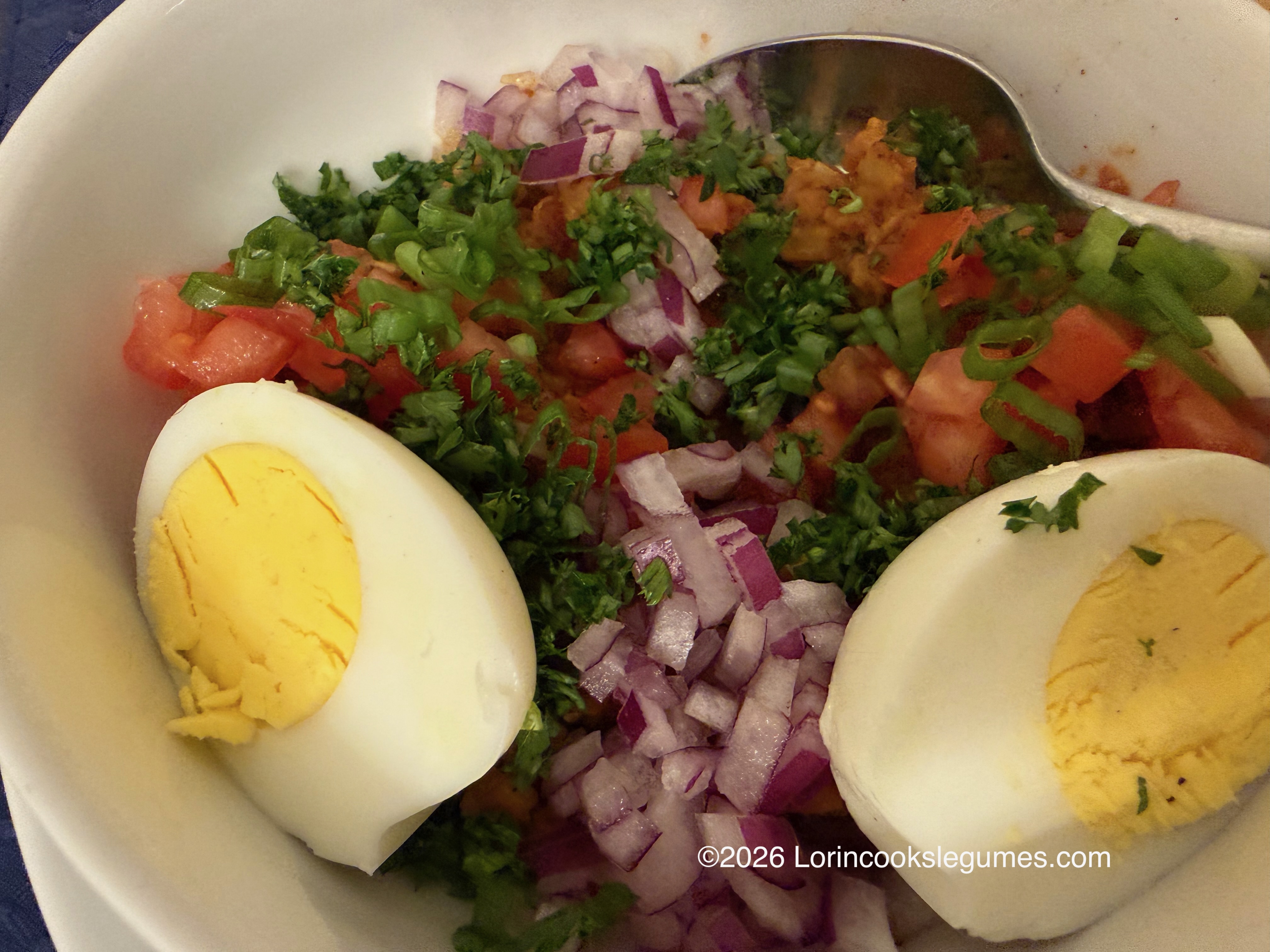 A bowl of mashed beans, with chopped vegetables, herbs, and hard-boiled eggs. ©2026 Lorincookslegumes.com