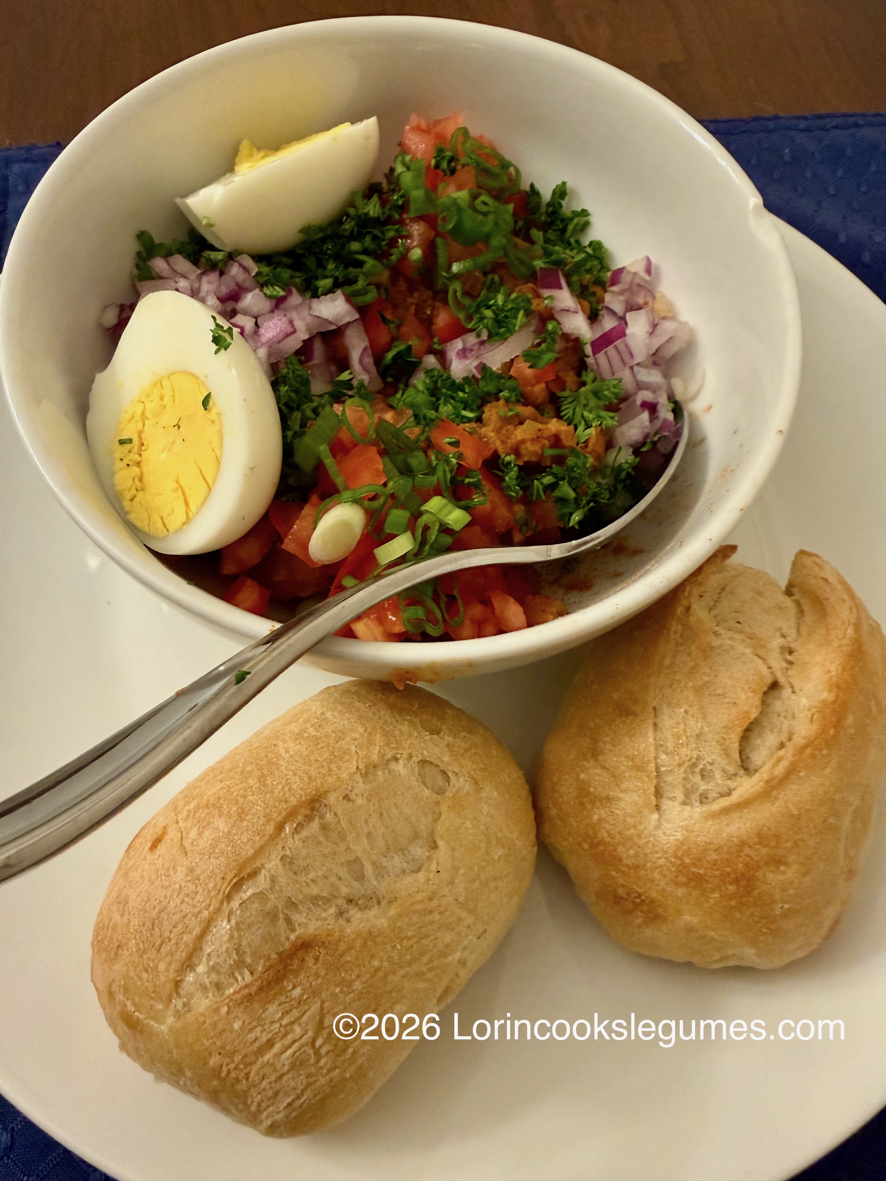 A bowl of mashed beans with fresh vegetables and boiled eggs, served with bread rolls. ©2026 Lorincookslegumes.com