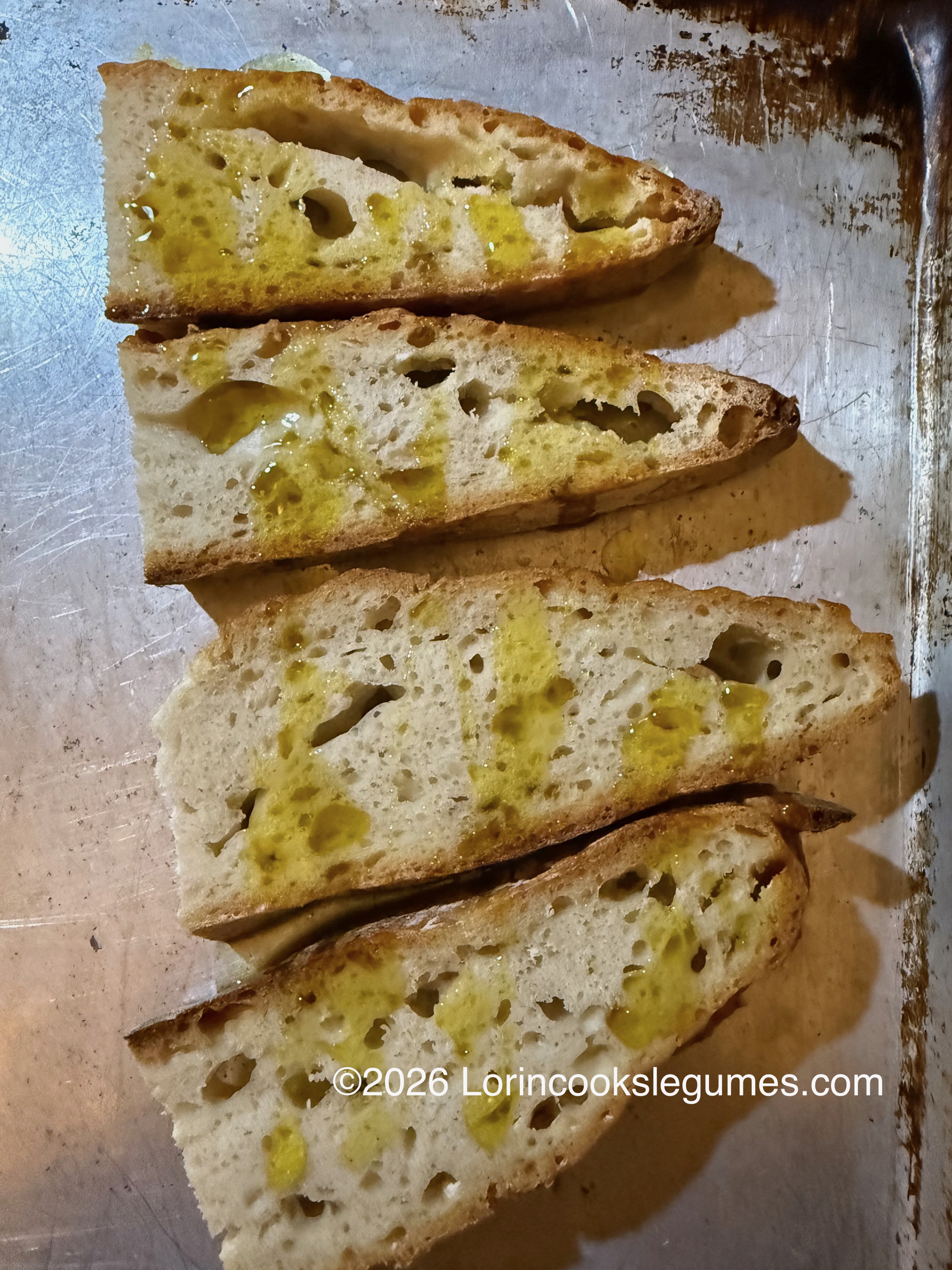 Four slices of bread drizzled with olive oil on a metal baking tray ready to be toasted.