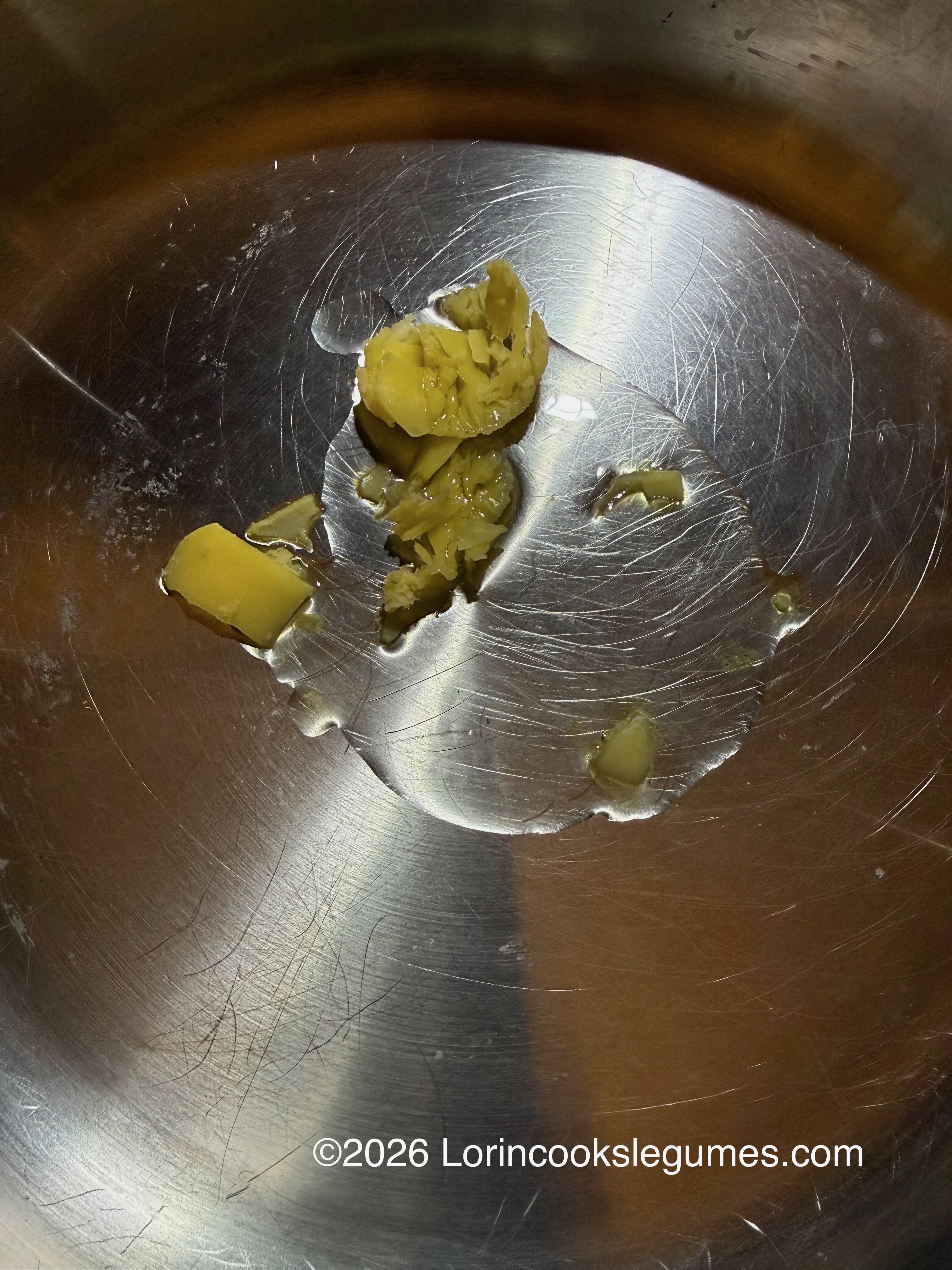 Small pieces of yellow ghee melting in a metal pan.