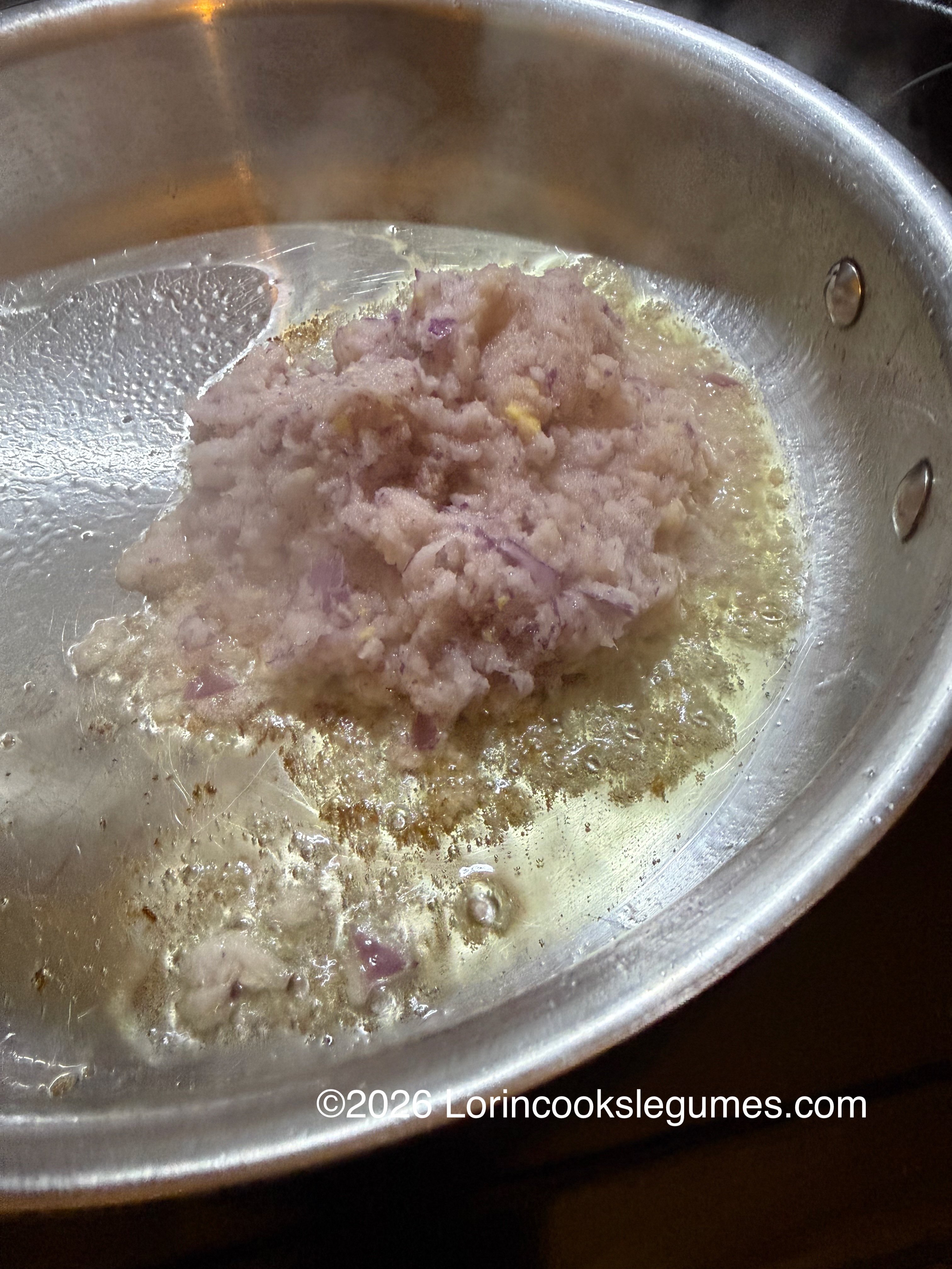Minced onions frying in hot oil in a stainless steel pan with steam rising