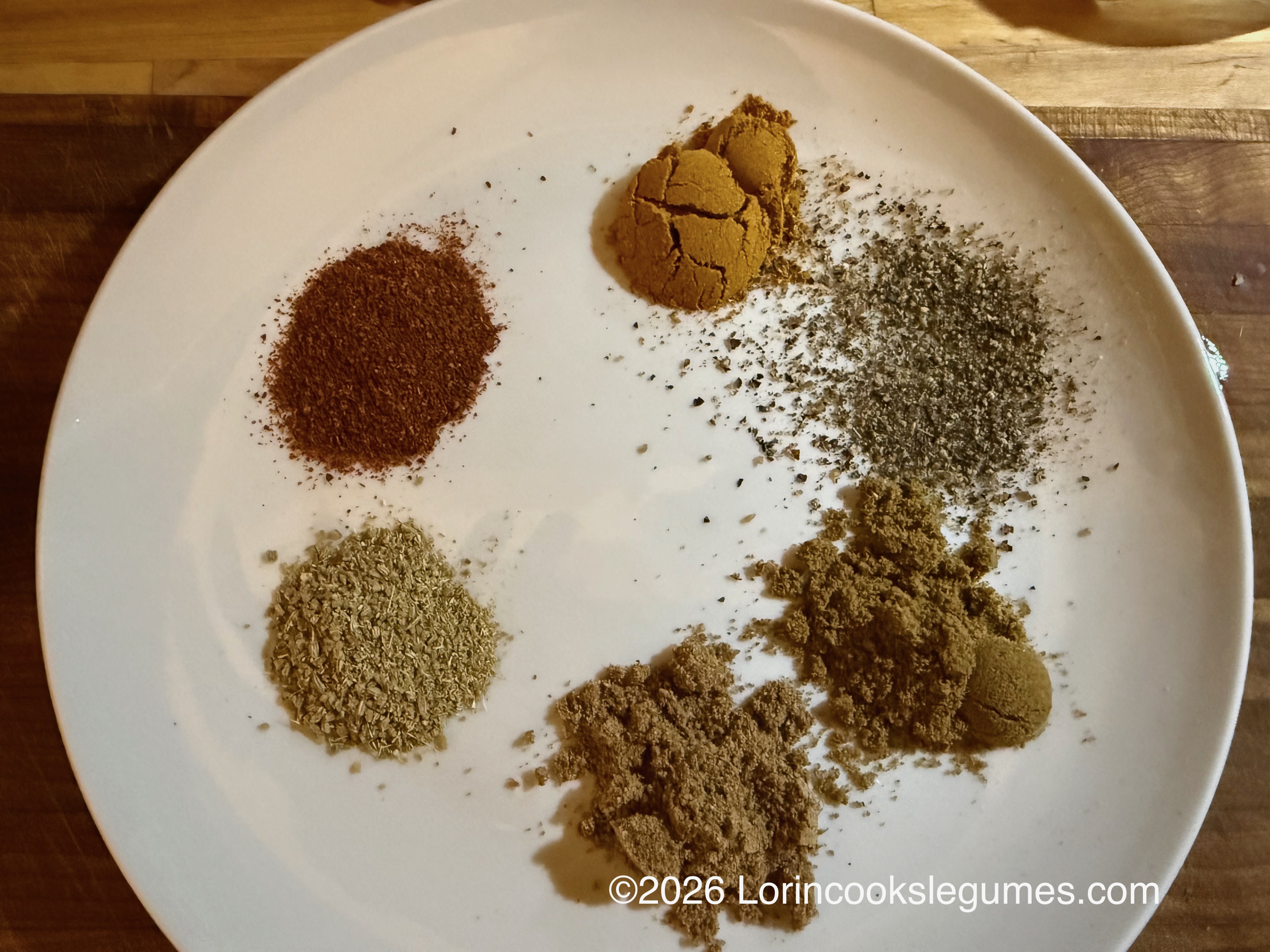 Several different ground spices arranged in a circle on a white plate
