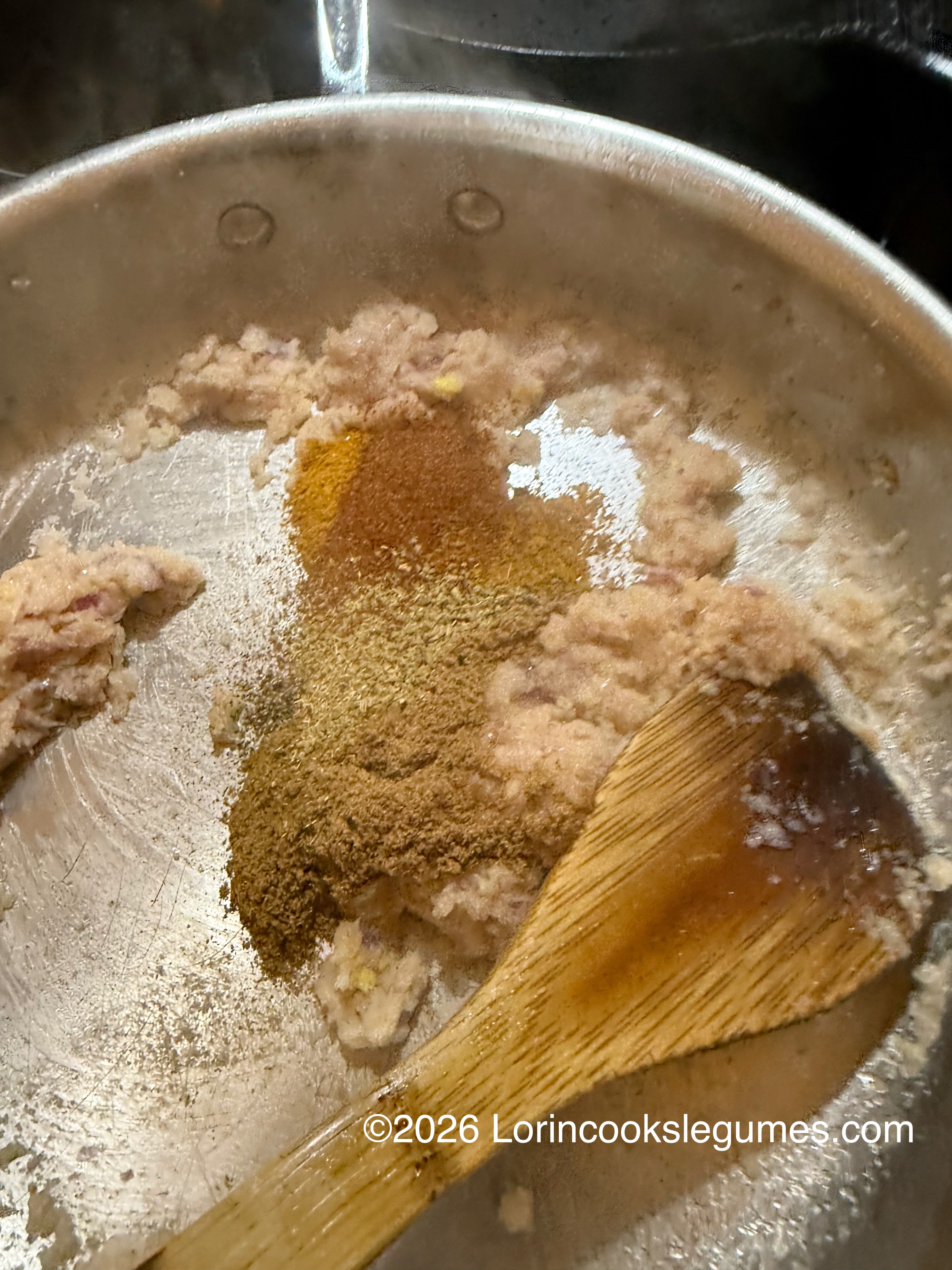 Cooking spices and minced onion in a pan with a wooden spatula