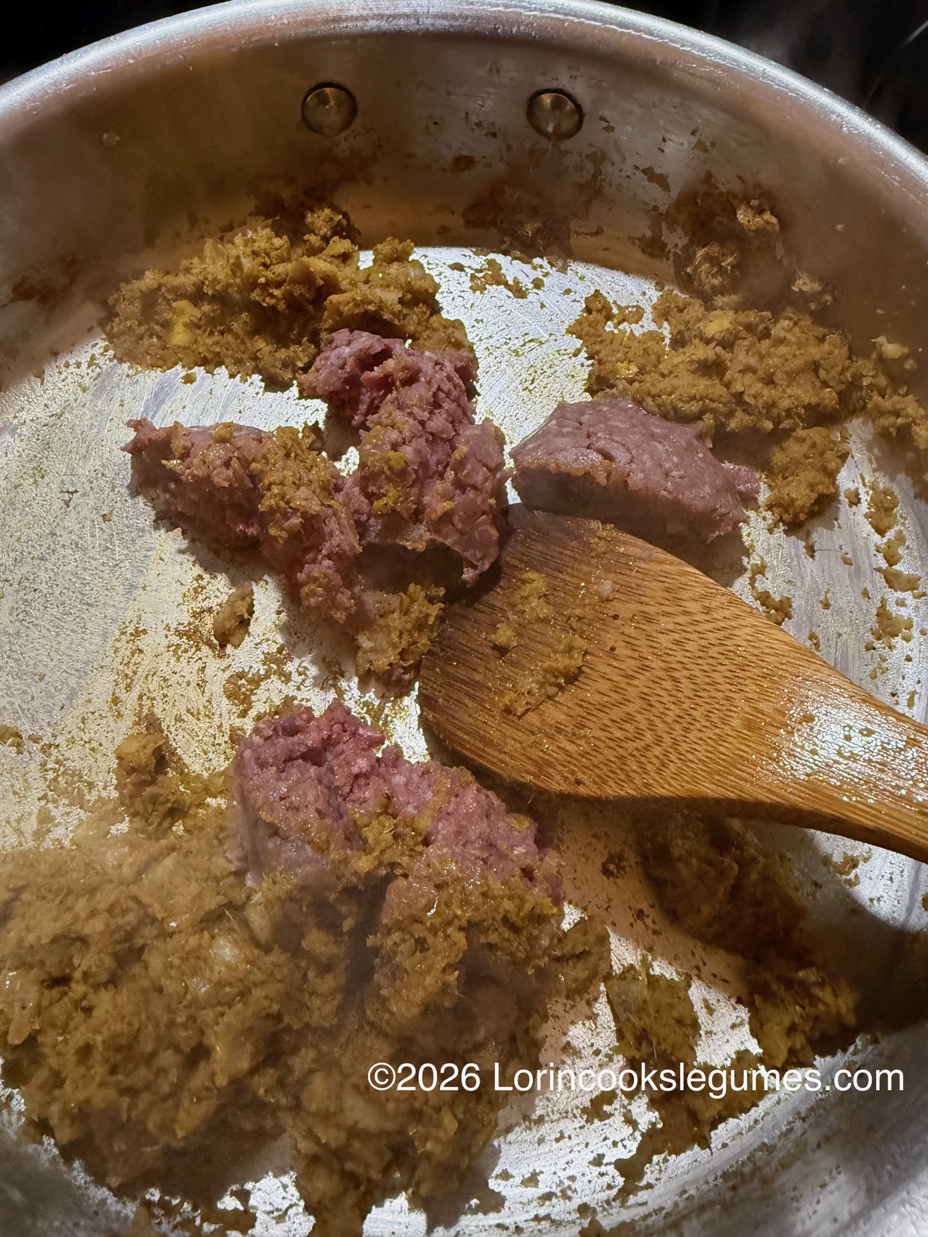Wooden spatula stirring ground meat and cooked onion and spices in a metal pan