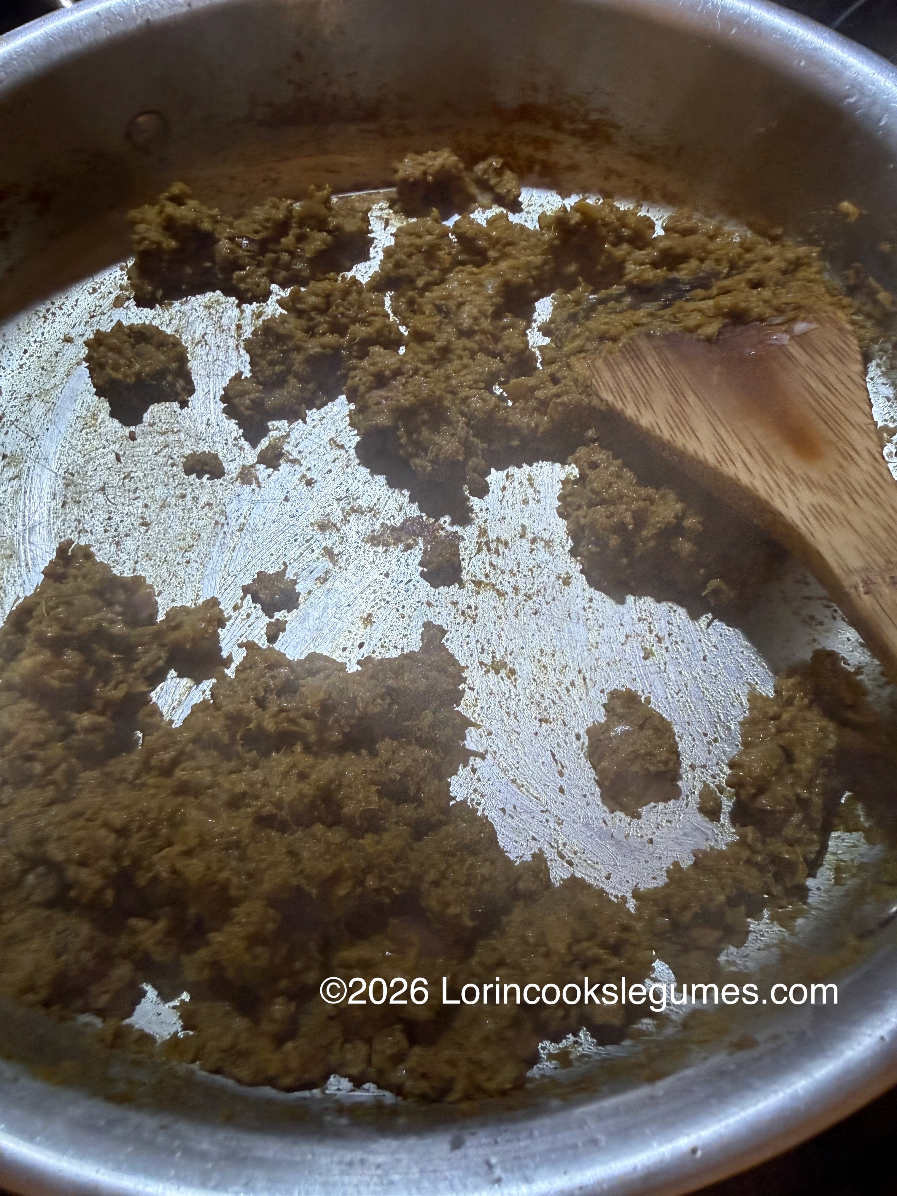 Brown curry paste cooking in a metal pan being stirred with a wooden spatula