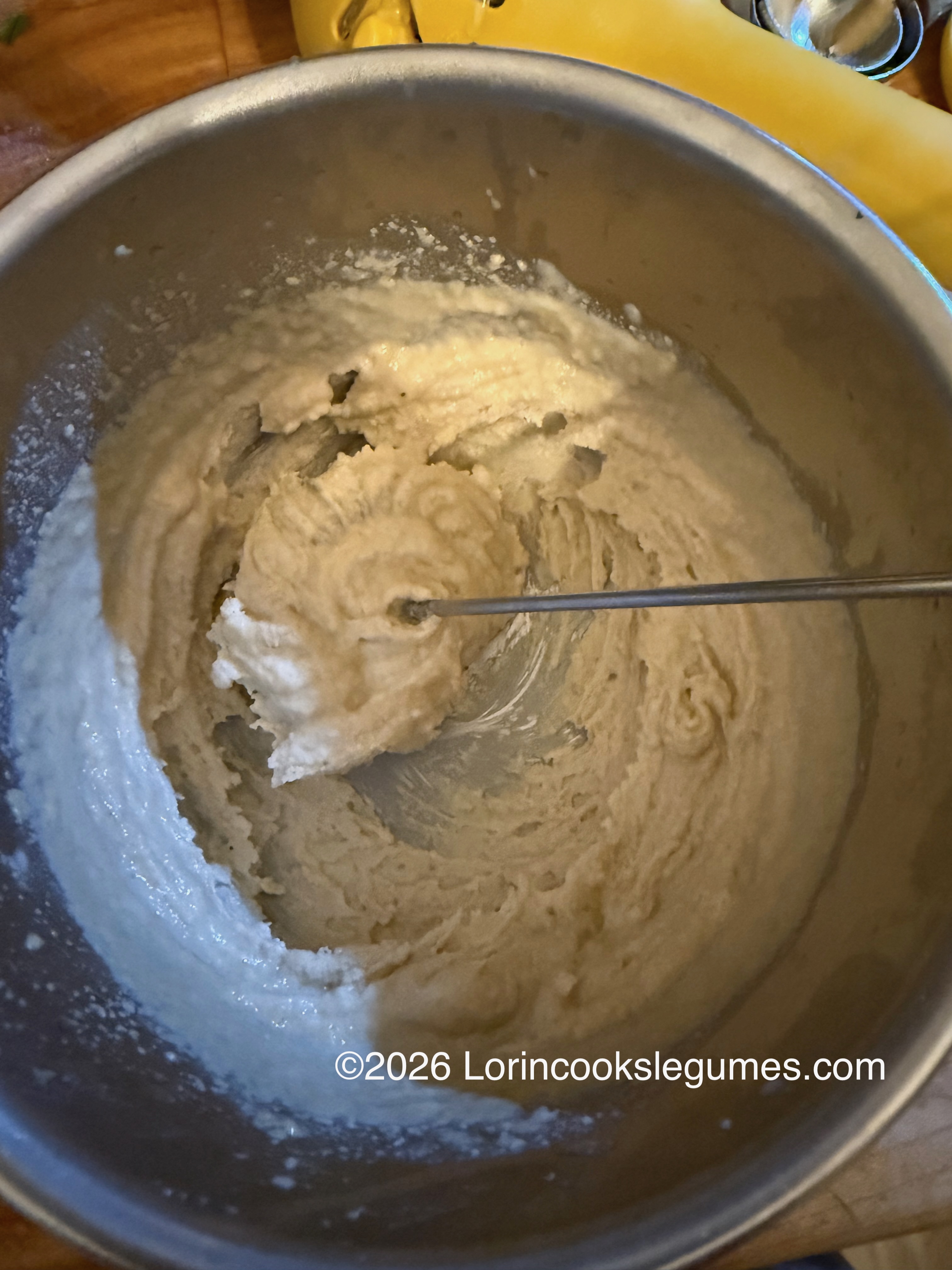 IMG_9954 A metal mixing bowl with a pale creamy mixture of tahini and lemon juice, being stirred by a whisk on a wooden surface
