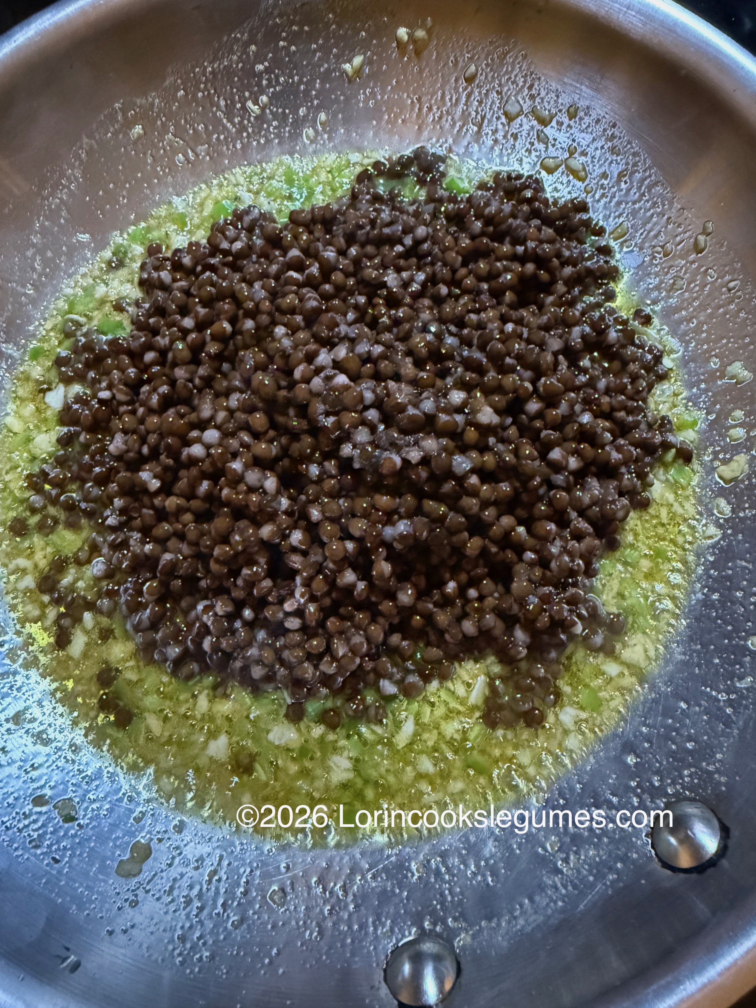 Black lentils cooking in oil with chopped garlic and green chilies in a metal pan