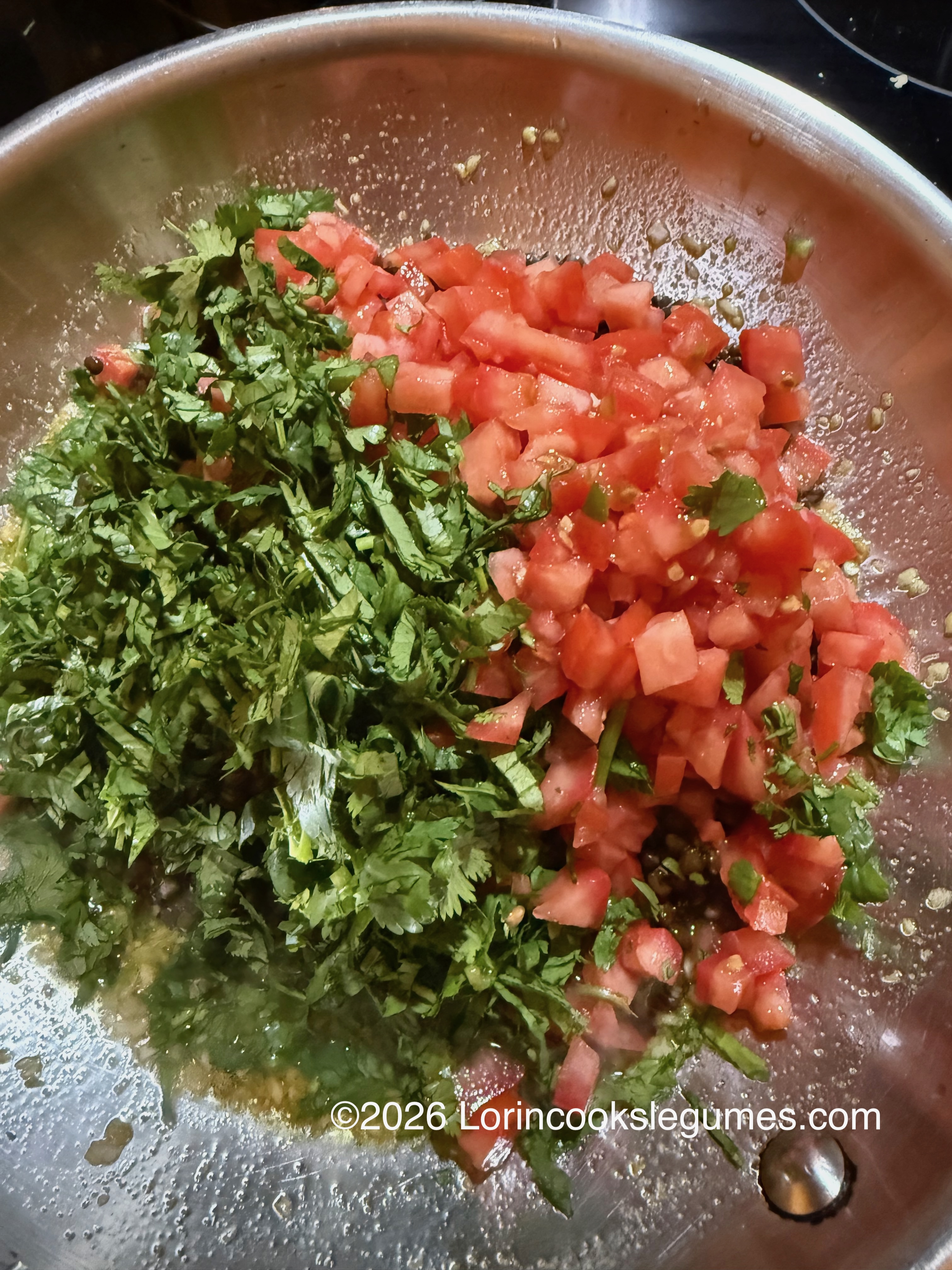 Chopped fresh cilantro and diced tomatoes on top of black lentils in a metal pan.