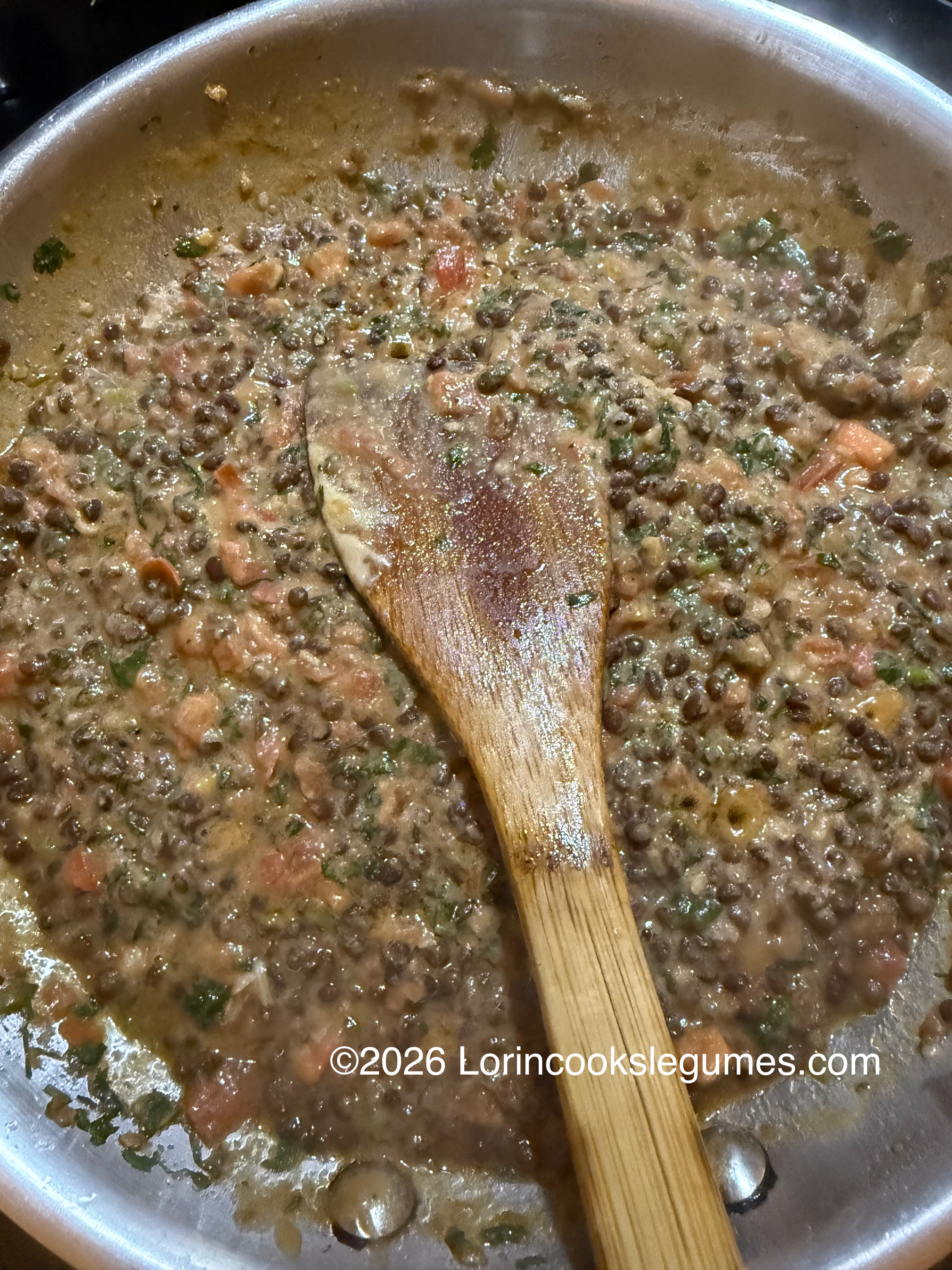 Lentil stew cooking in a pan with a wooden spoon stirring
