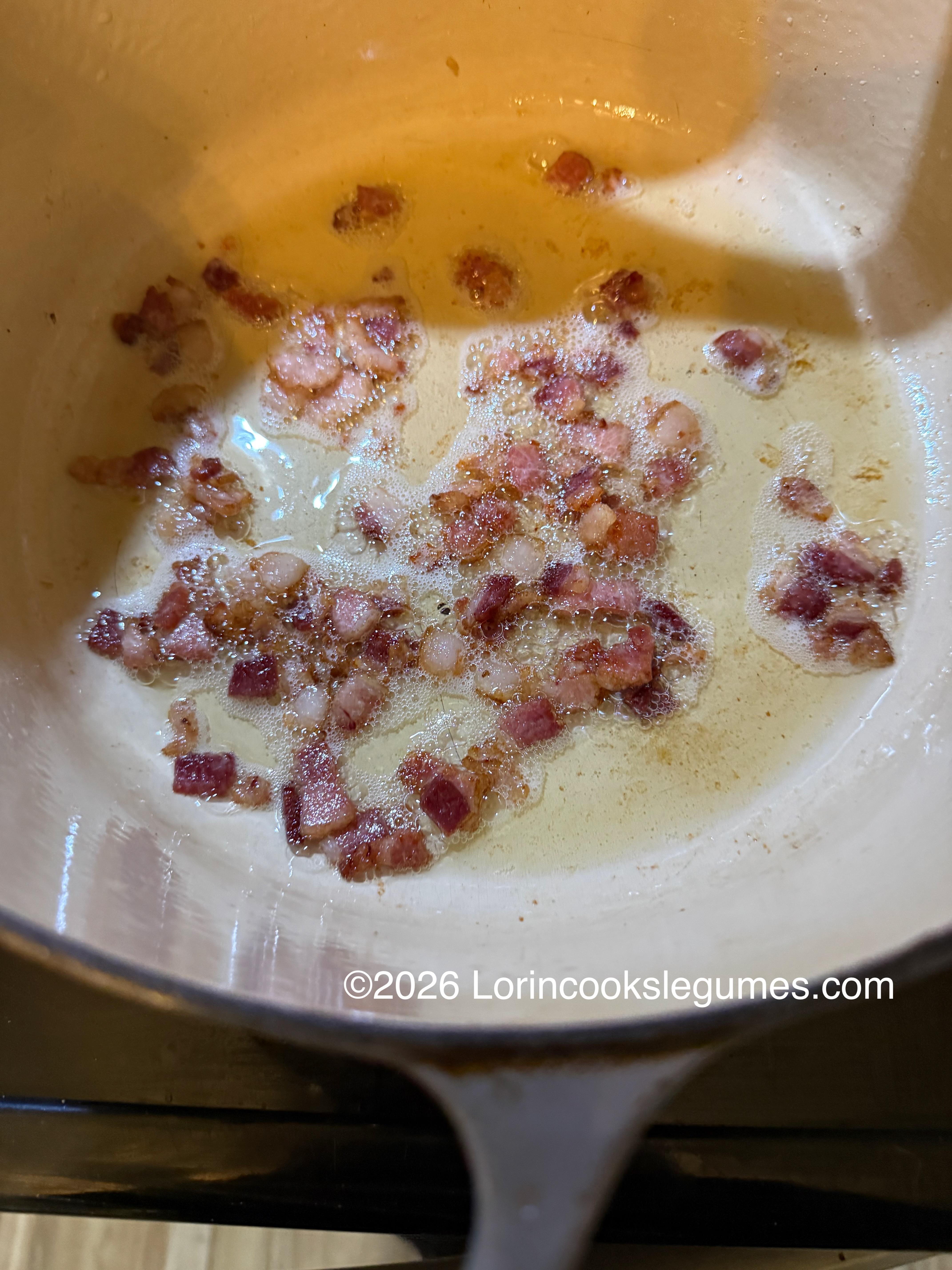 Bacon pieces frying in oil inside a cast iron pot.