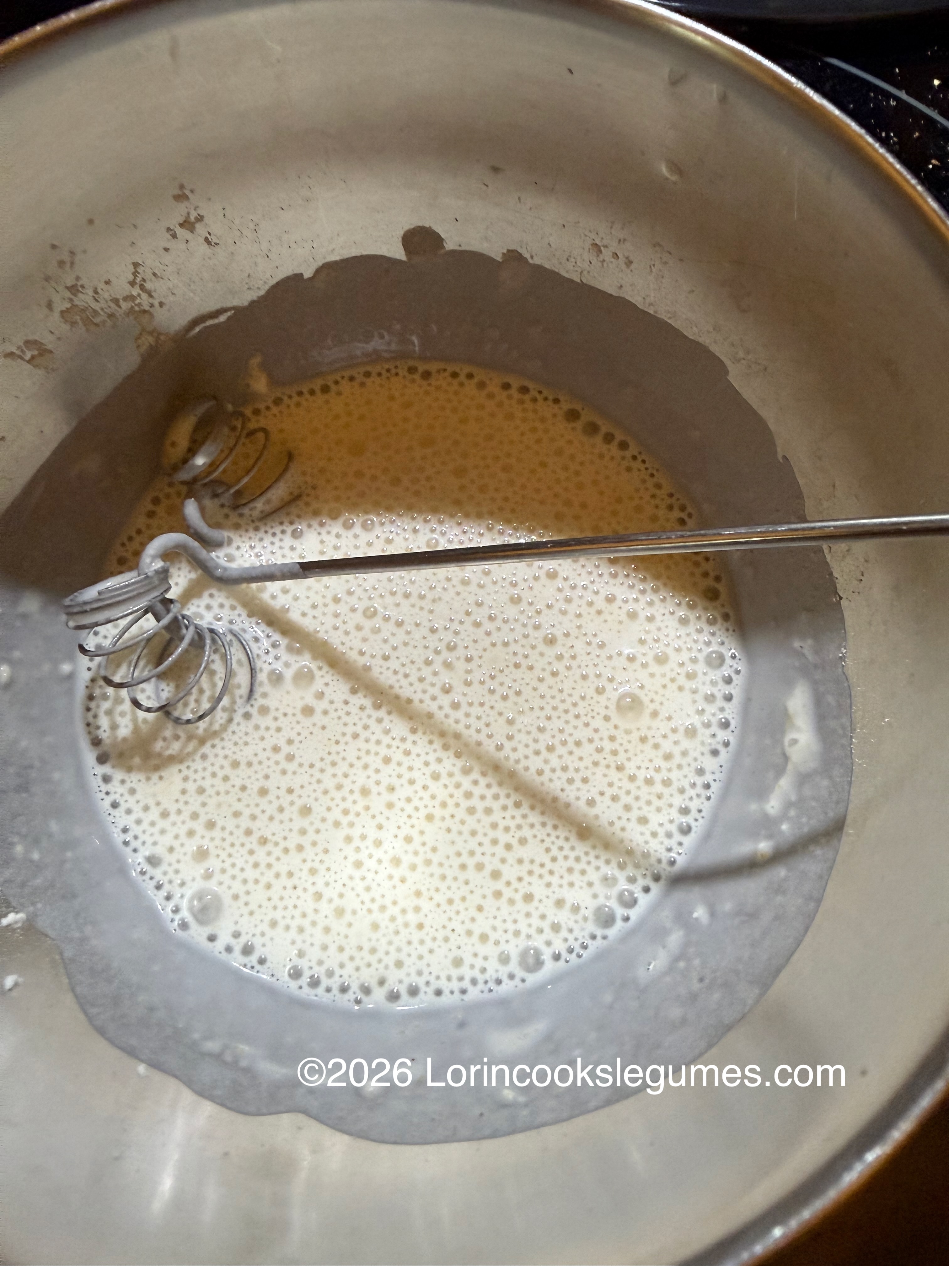 Whisk stirring frothy batter in a metal bowl