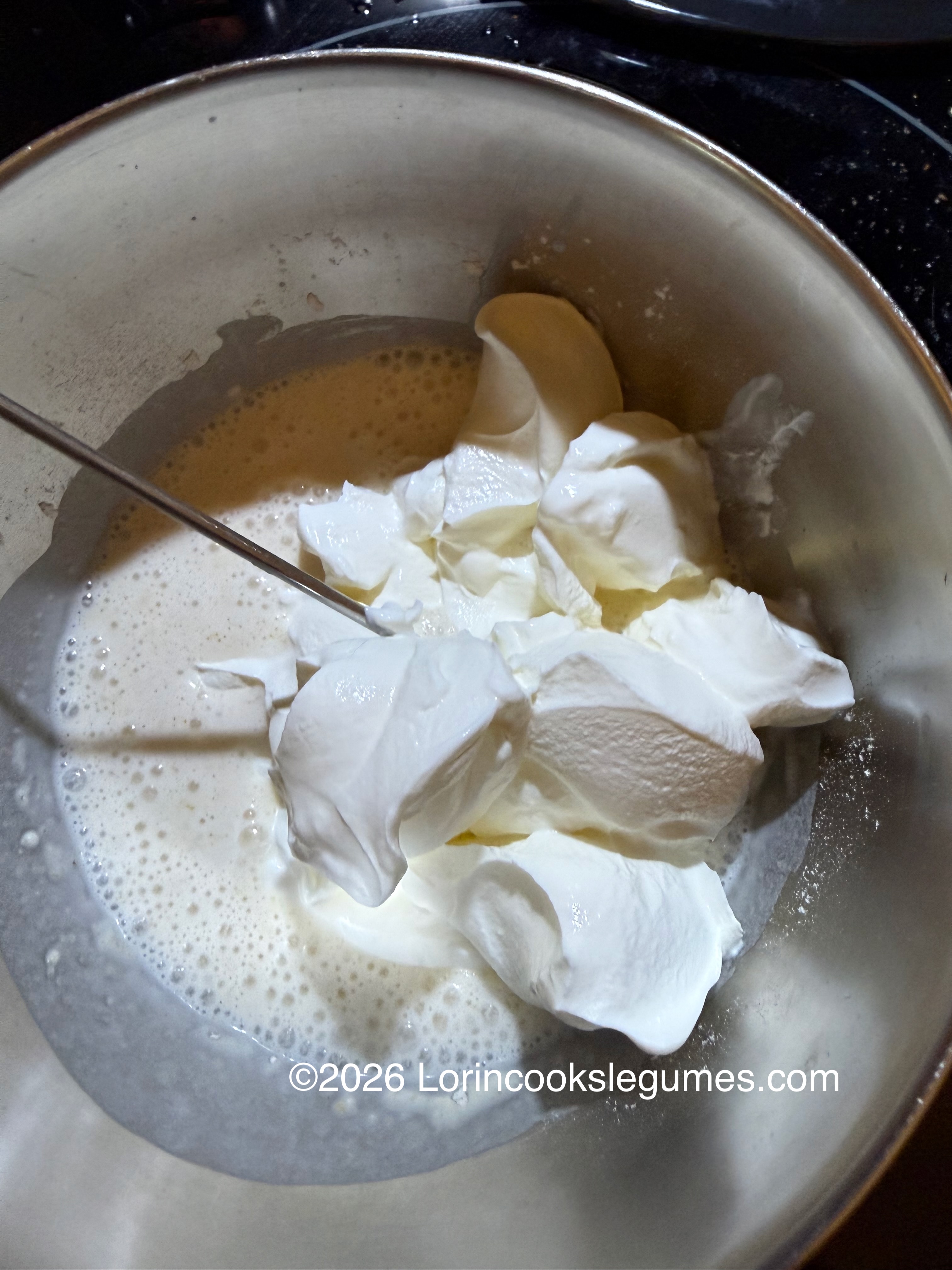 Metal bowl with batter and dollops of sour cream being mixed with a metal whisk.