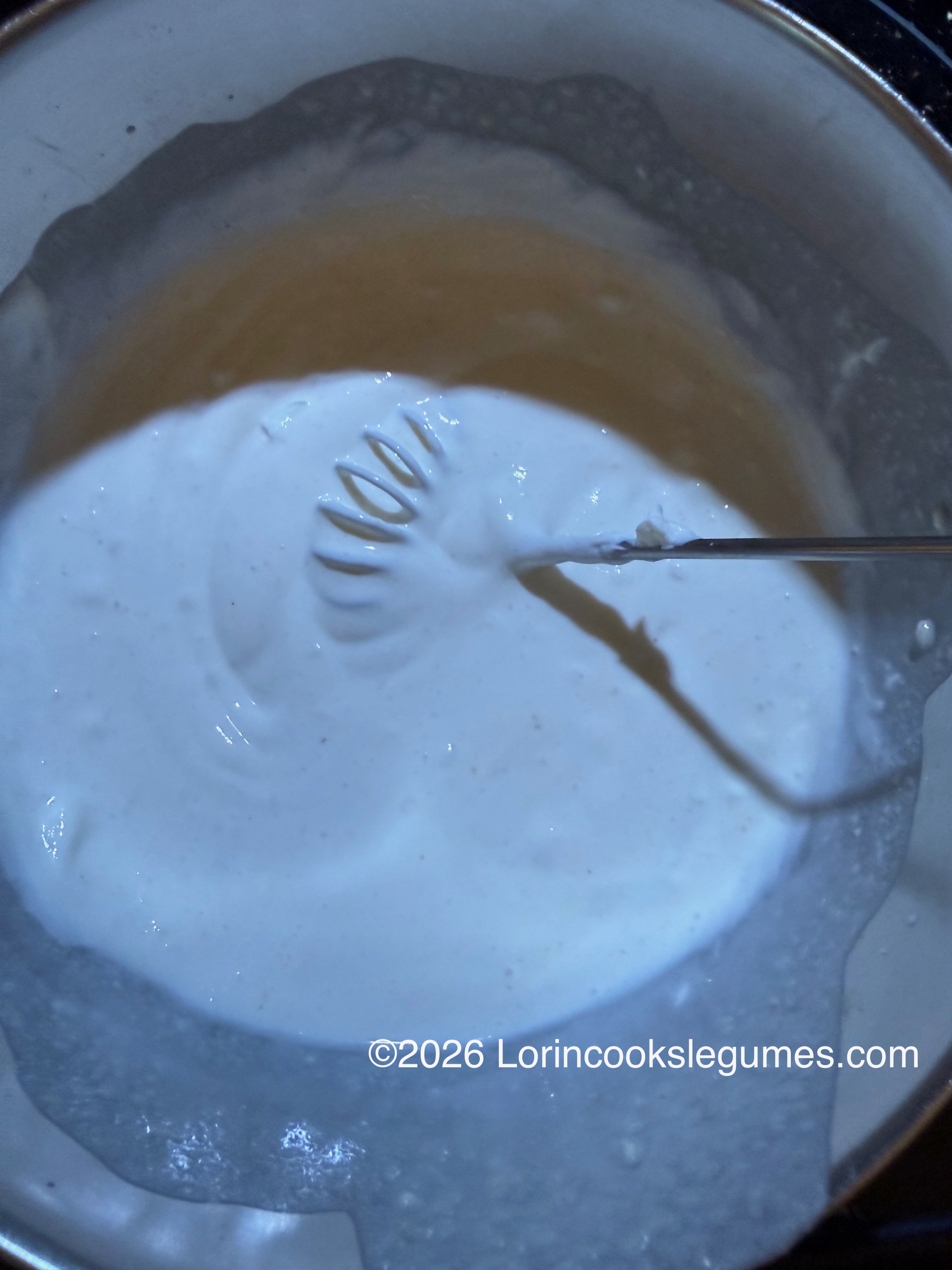 Whisk stirring white batter in a metal bowl