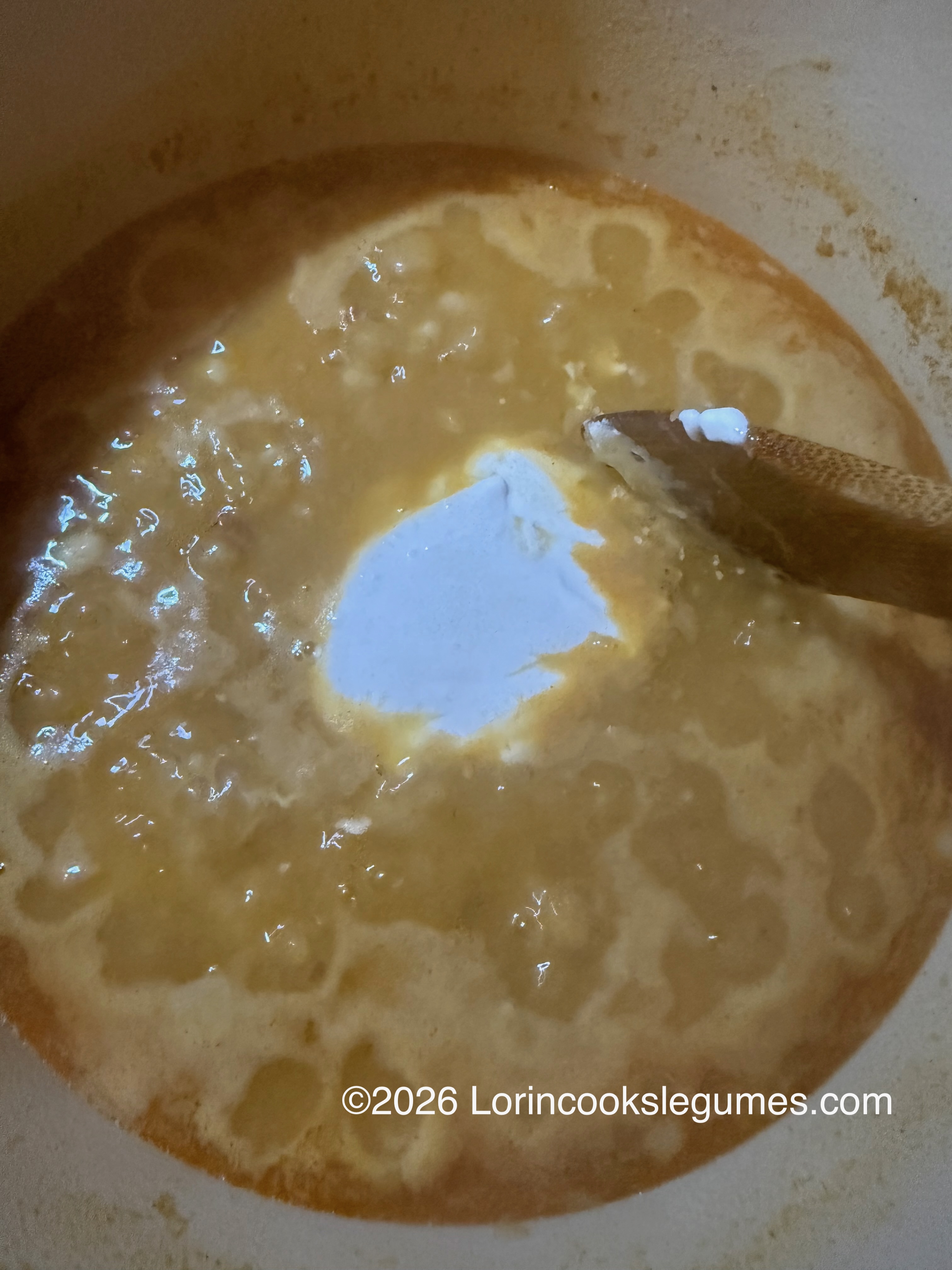 Wooden spoon stirring a bubbling pot of soup with cream added