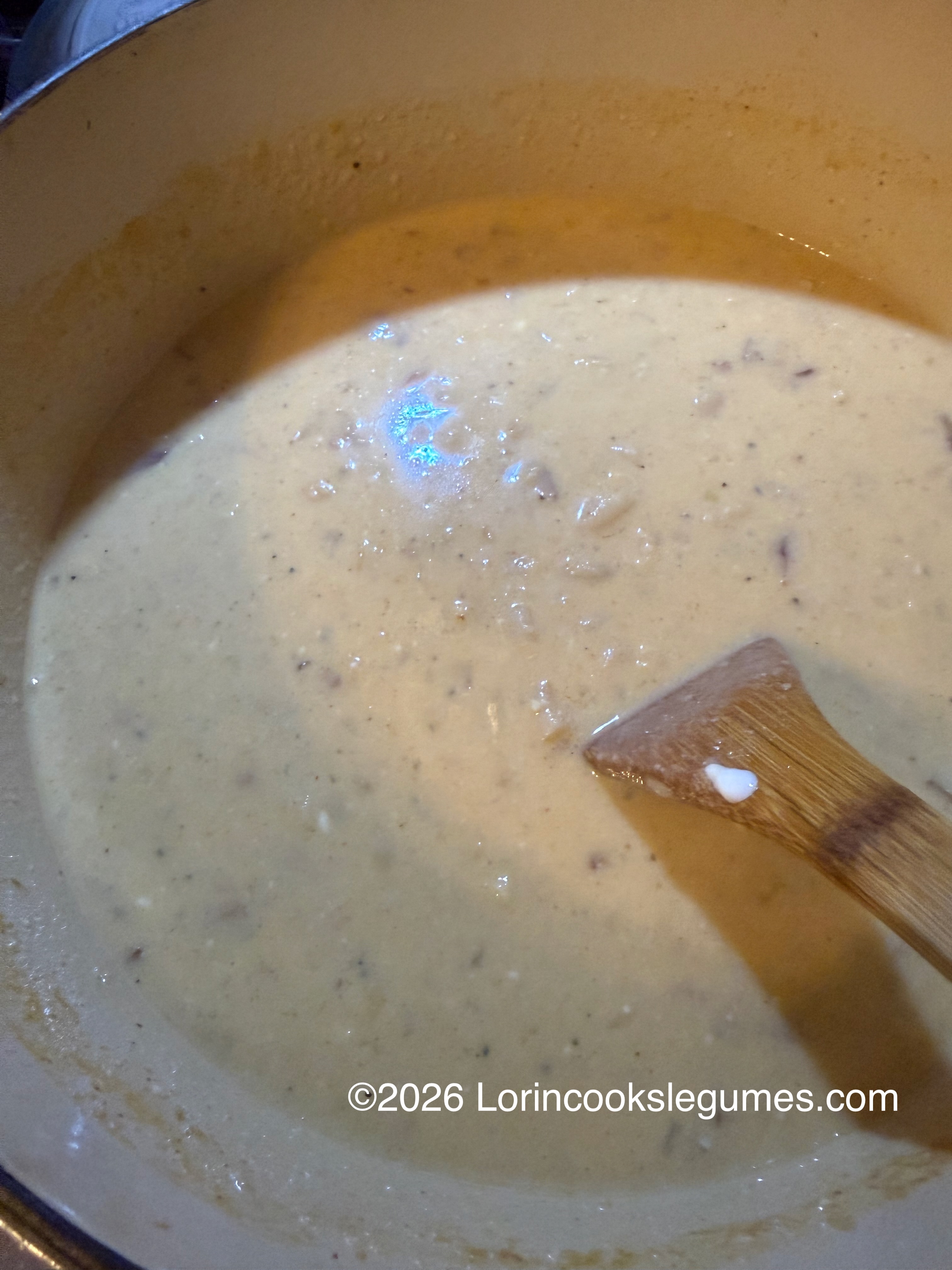 Creamy bean soup with small chunks being stirred by a wooden spoon in a pot