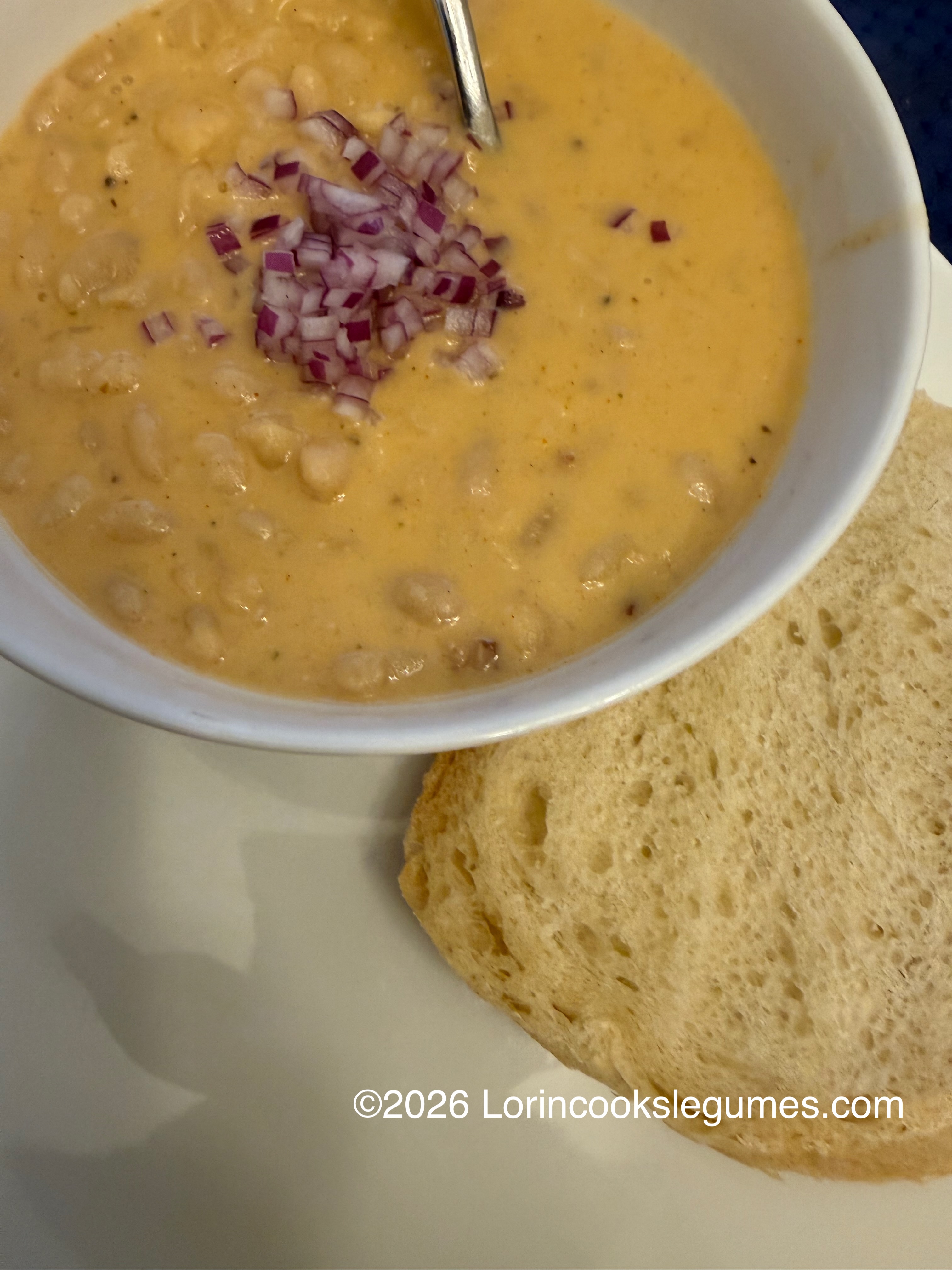 Bowl of creamy bean soup garnished with chopped red onions served with slices of bread