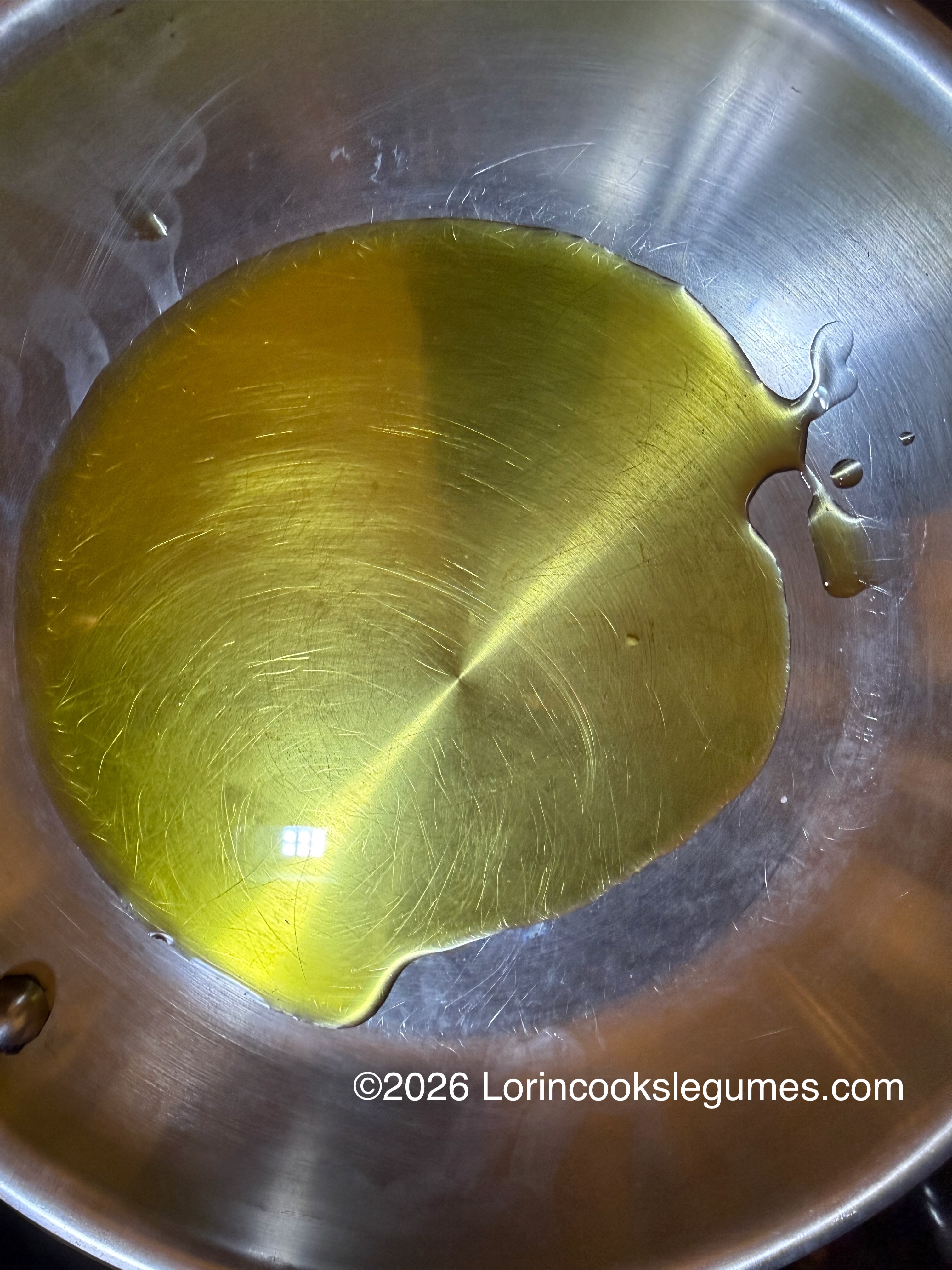 Golden olive oil pooled in the center of a stainless steel pan