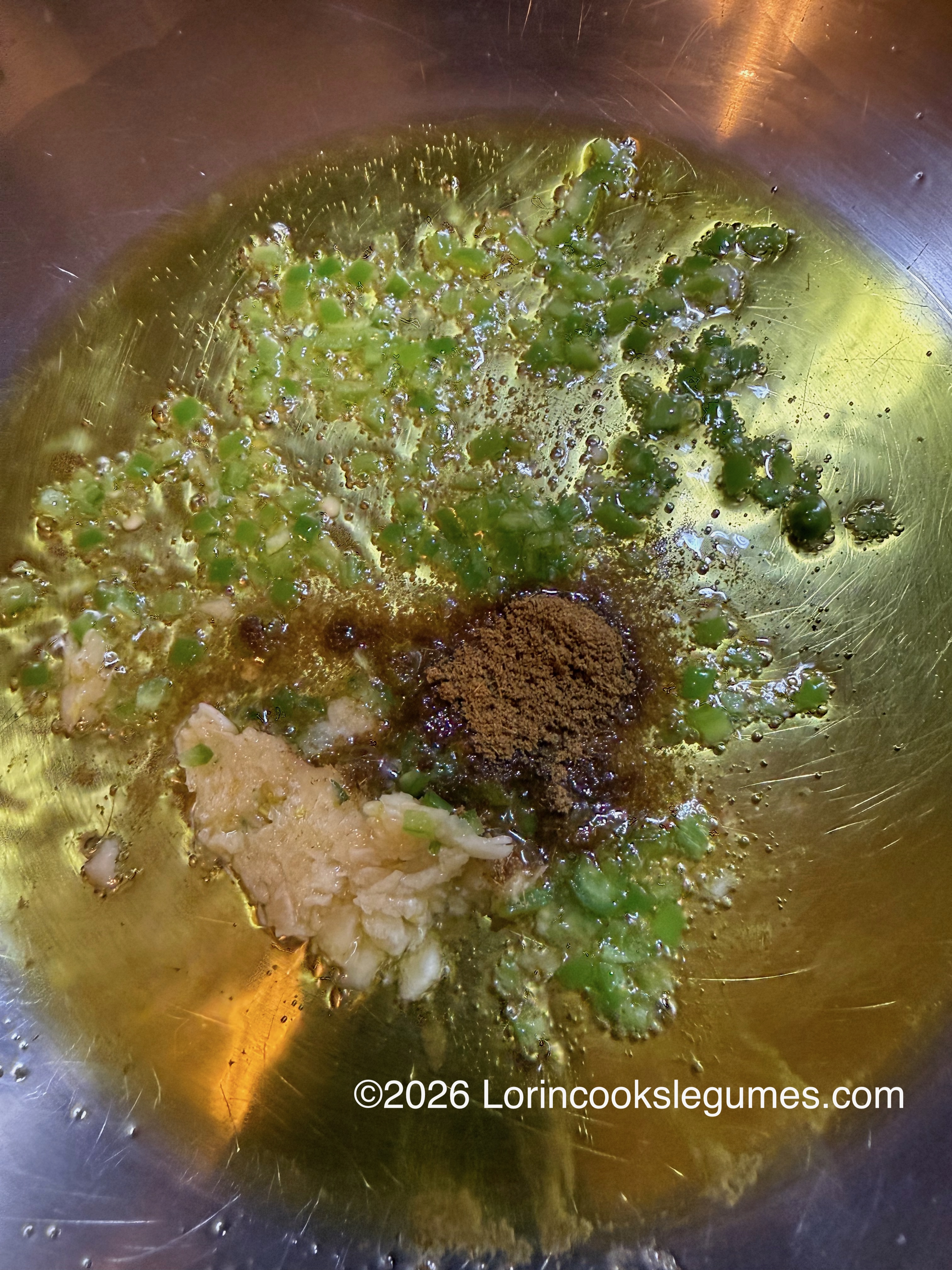 Oil heating in a pan with minced garlic, chopped green chilies, and ground cumin.