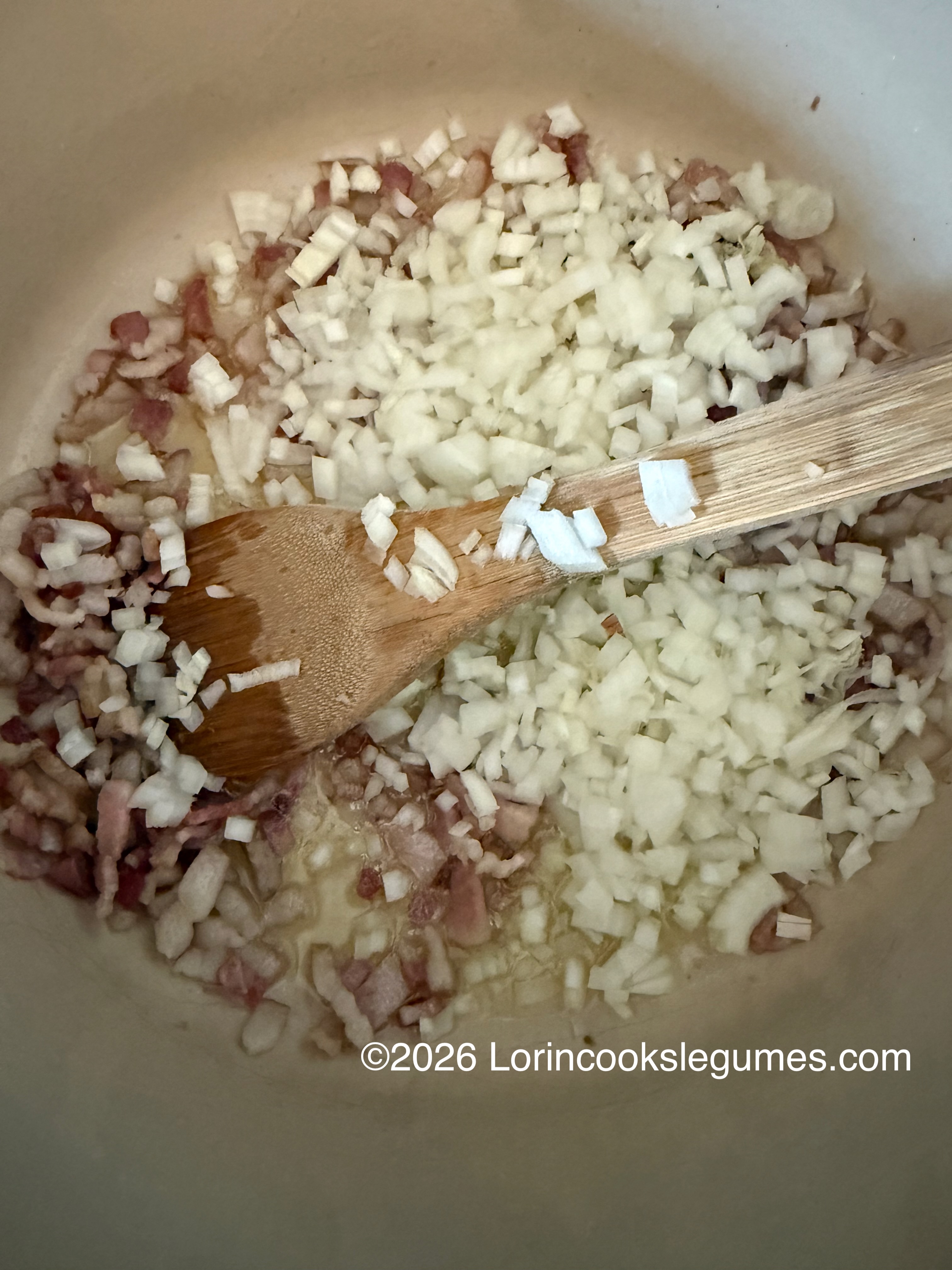 Diced onions and bacon cooking in a pot with a wooden spatula