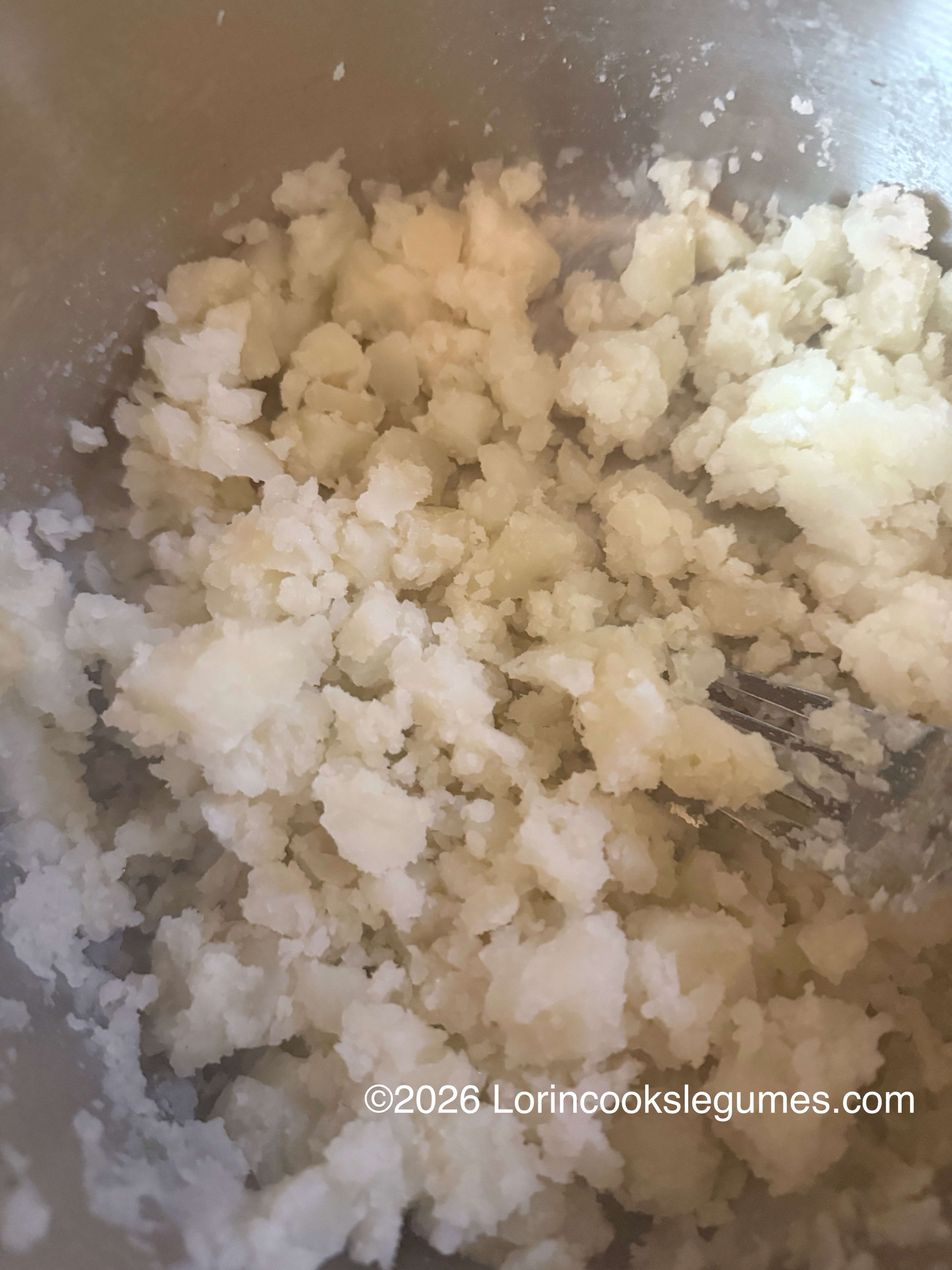 Close-up of crumbled roughly mashed potatoes in a metal bowl with a fork
