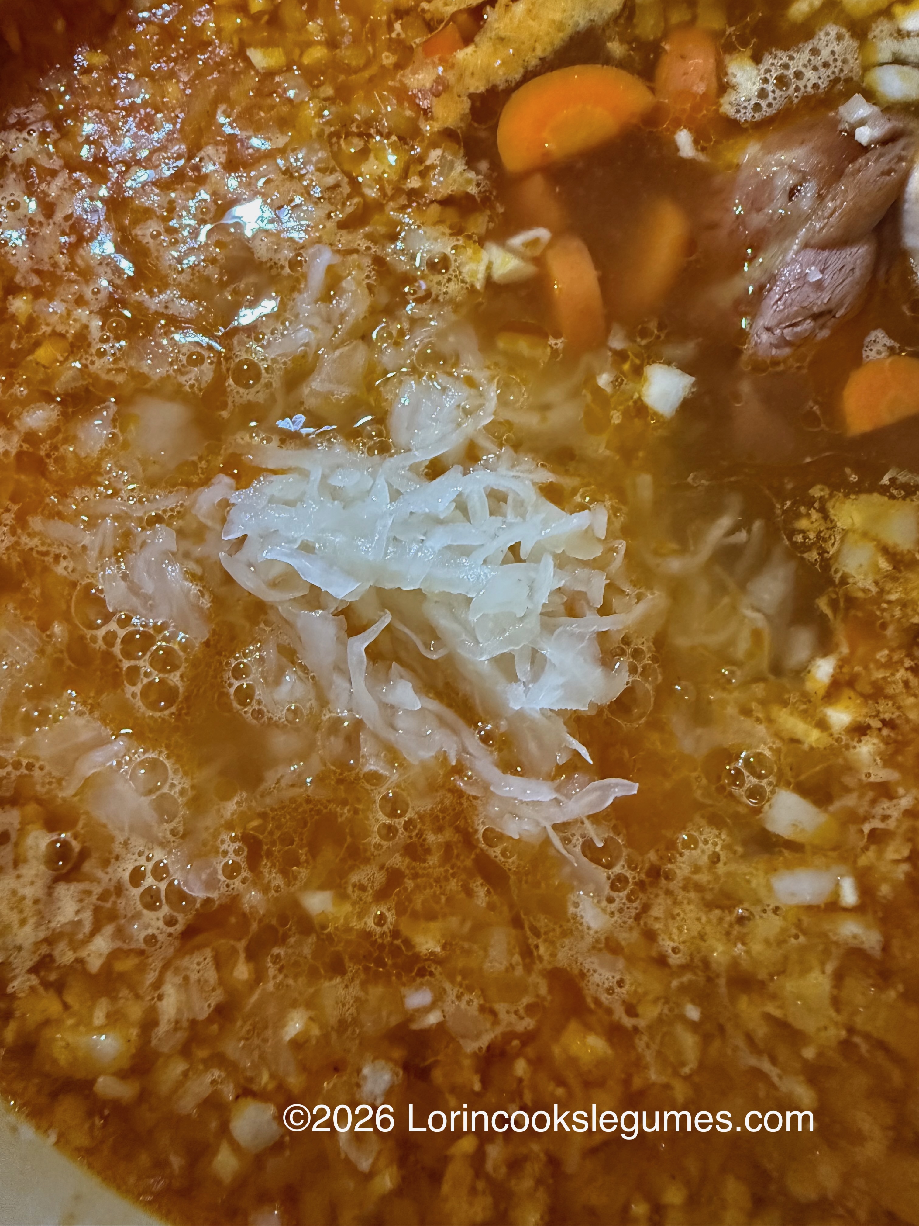 Close-up of simmering soup with visible carrots, meat, and shredded sauerkraut.
