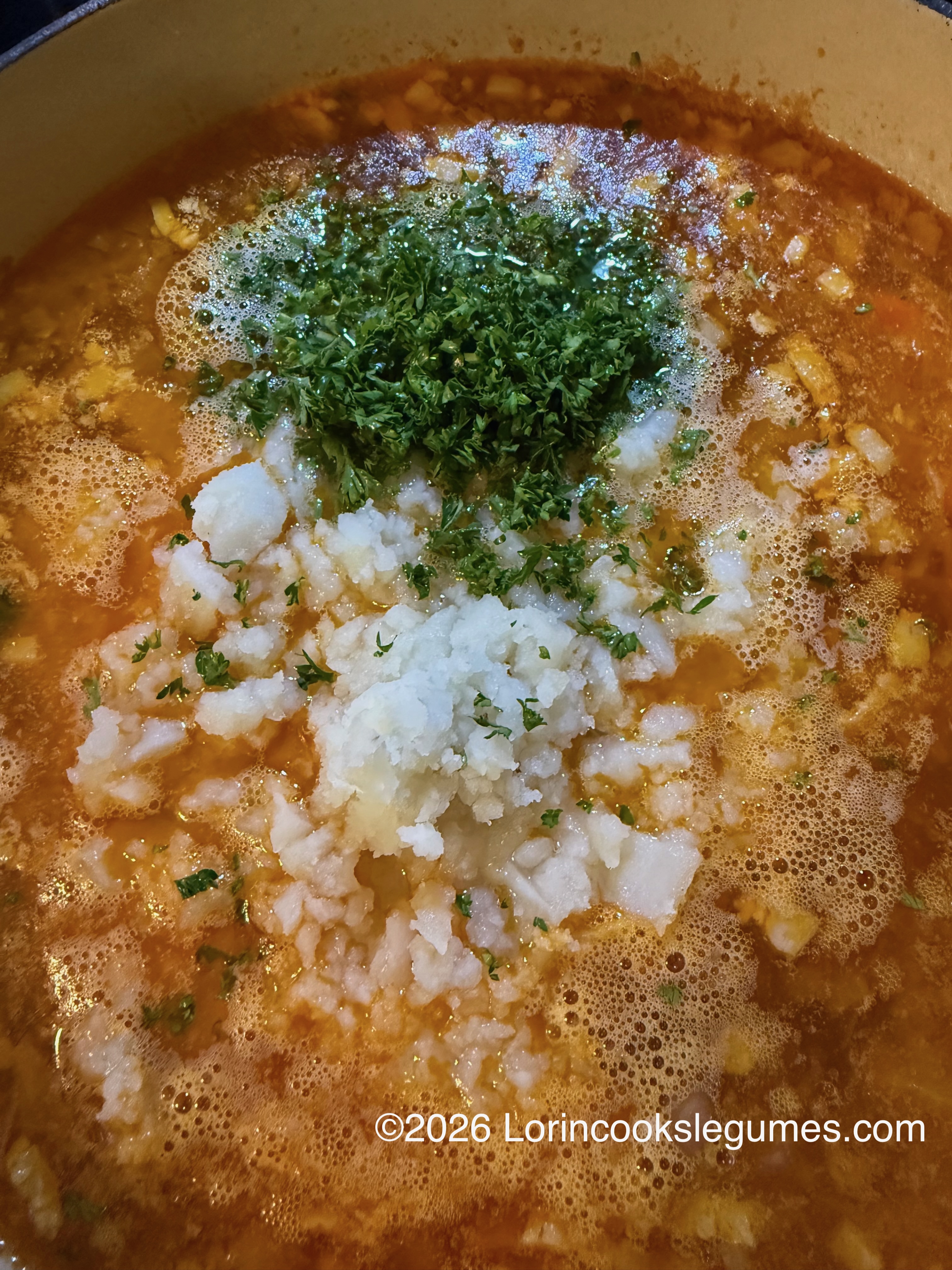 Chopped parsley and mashed potatoes added to simmering orange broth with diced onions