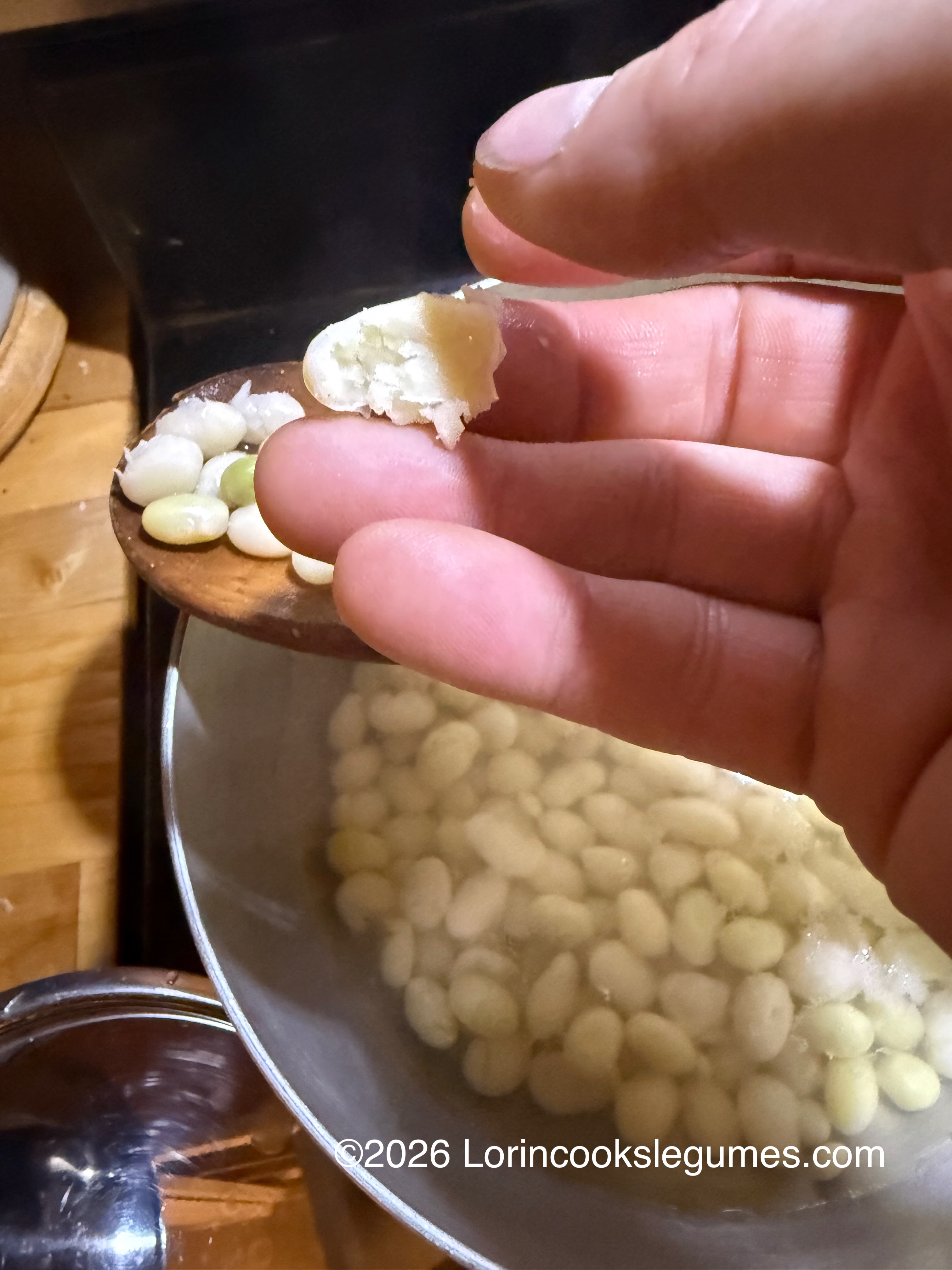 IMG_0264 Close-up of a hand holding smashed bean over a pot of beans, showing that the beans are fully cooked.